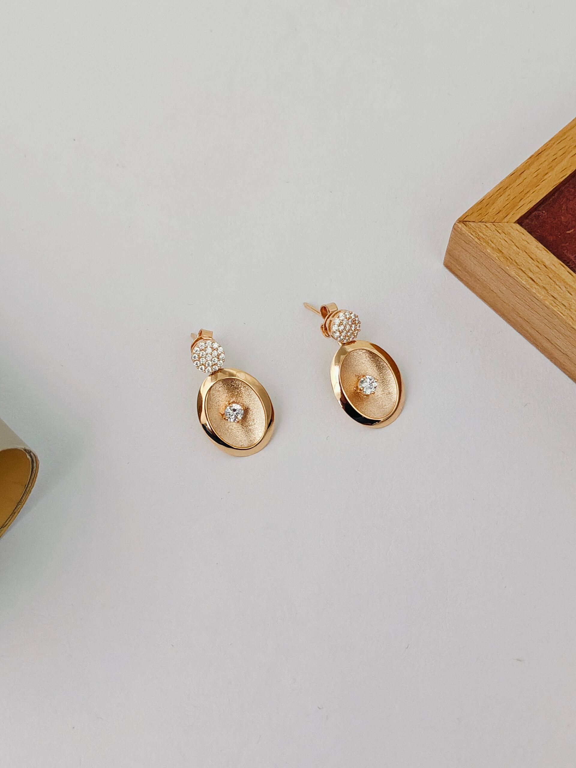 Gold earrings with gemstones on a light gray surface