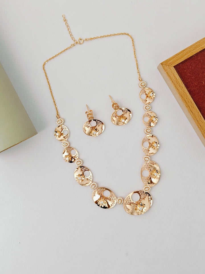 Gold necklace and earrings set on a light gray surface with a wooden box in the background.
