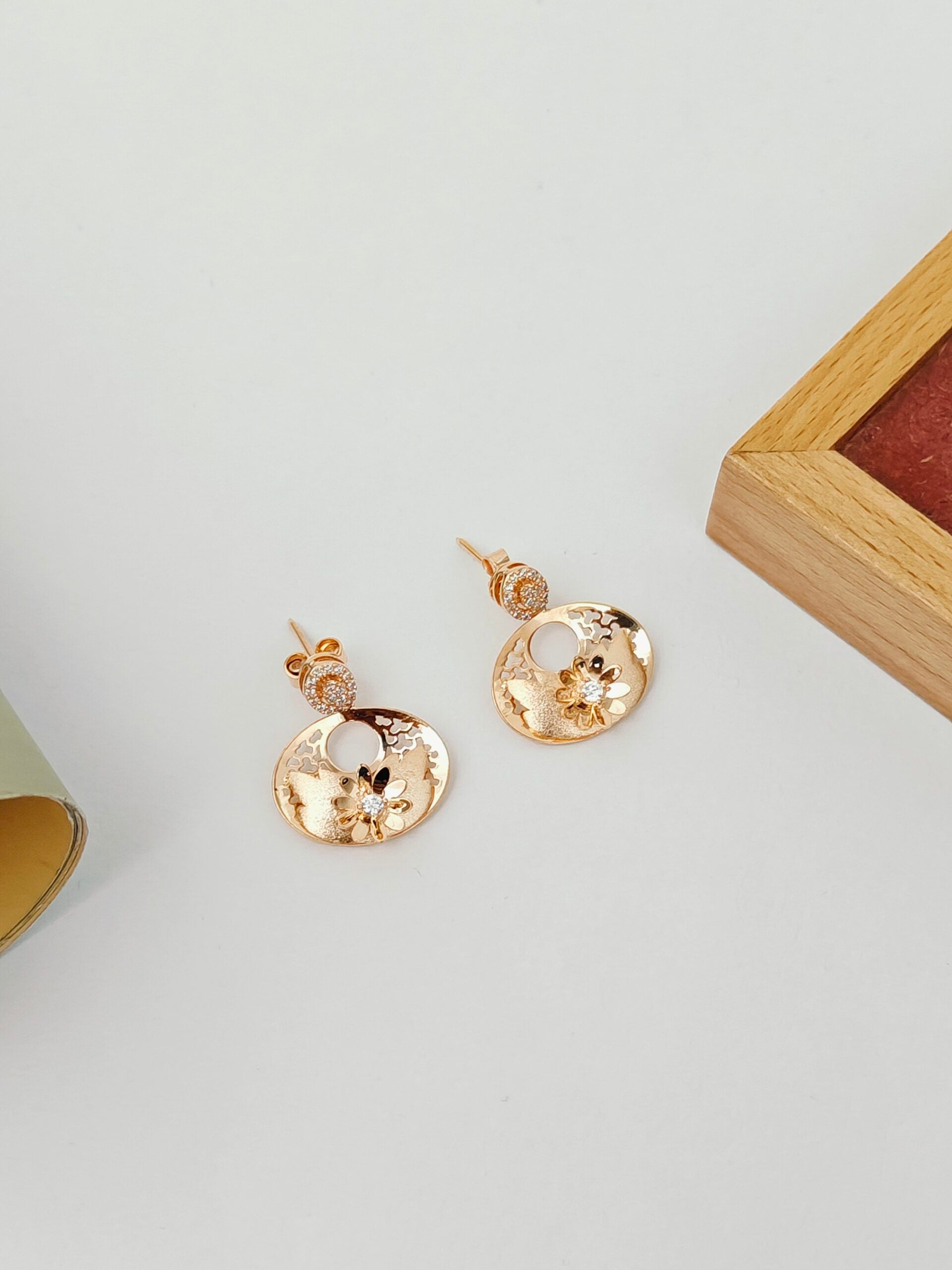Gold earrings on a light gray surface with a wooden box in the background