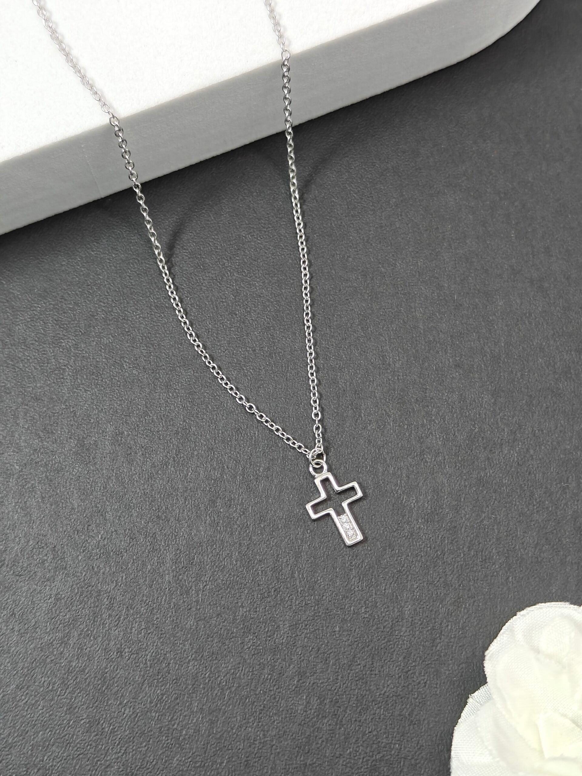 Silver cross necklace on a gray surface with a white flower