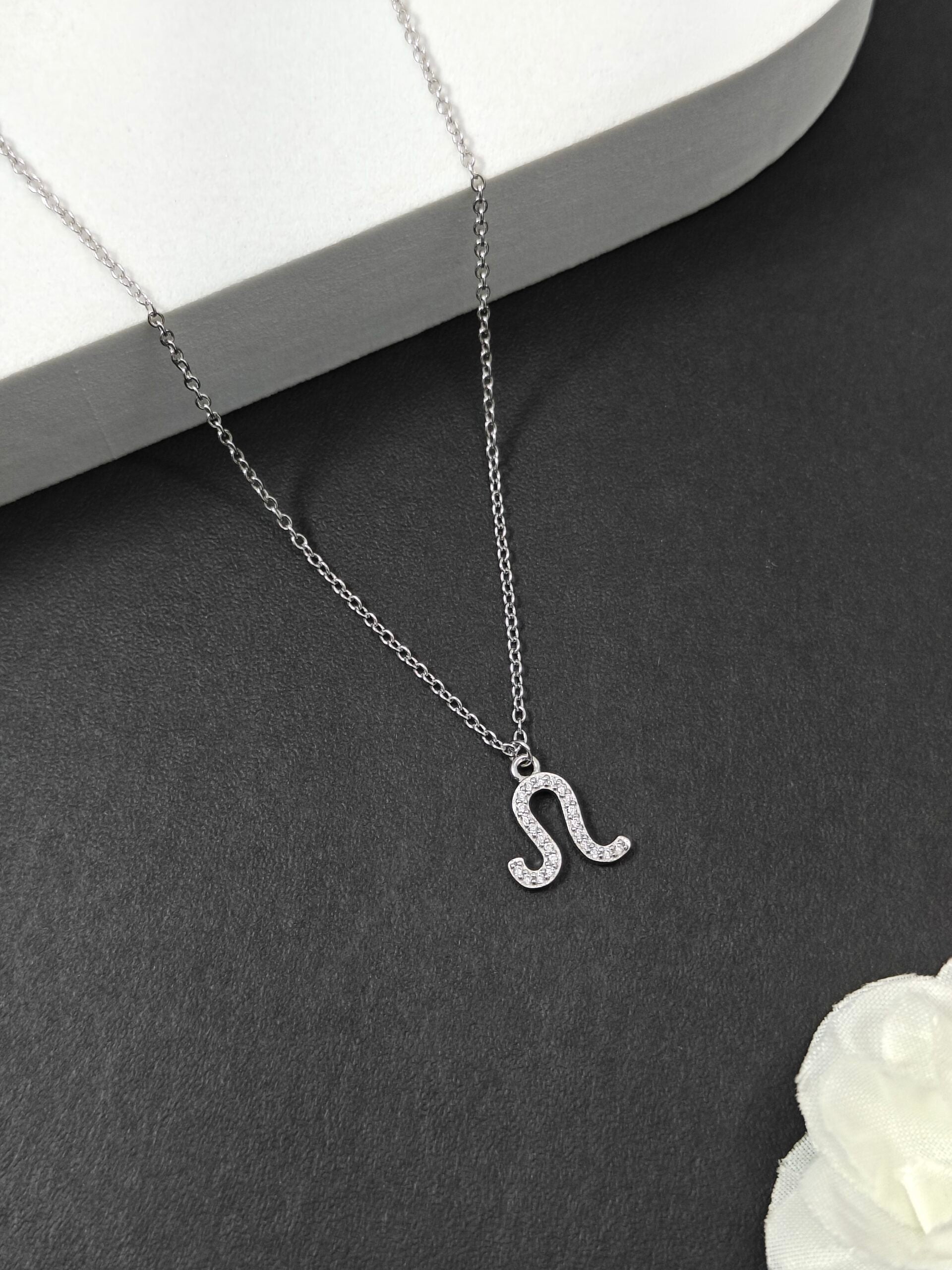 Silver necklace with a 'S' pendant on a dark surface with a white flower.