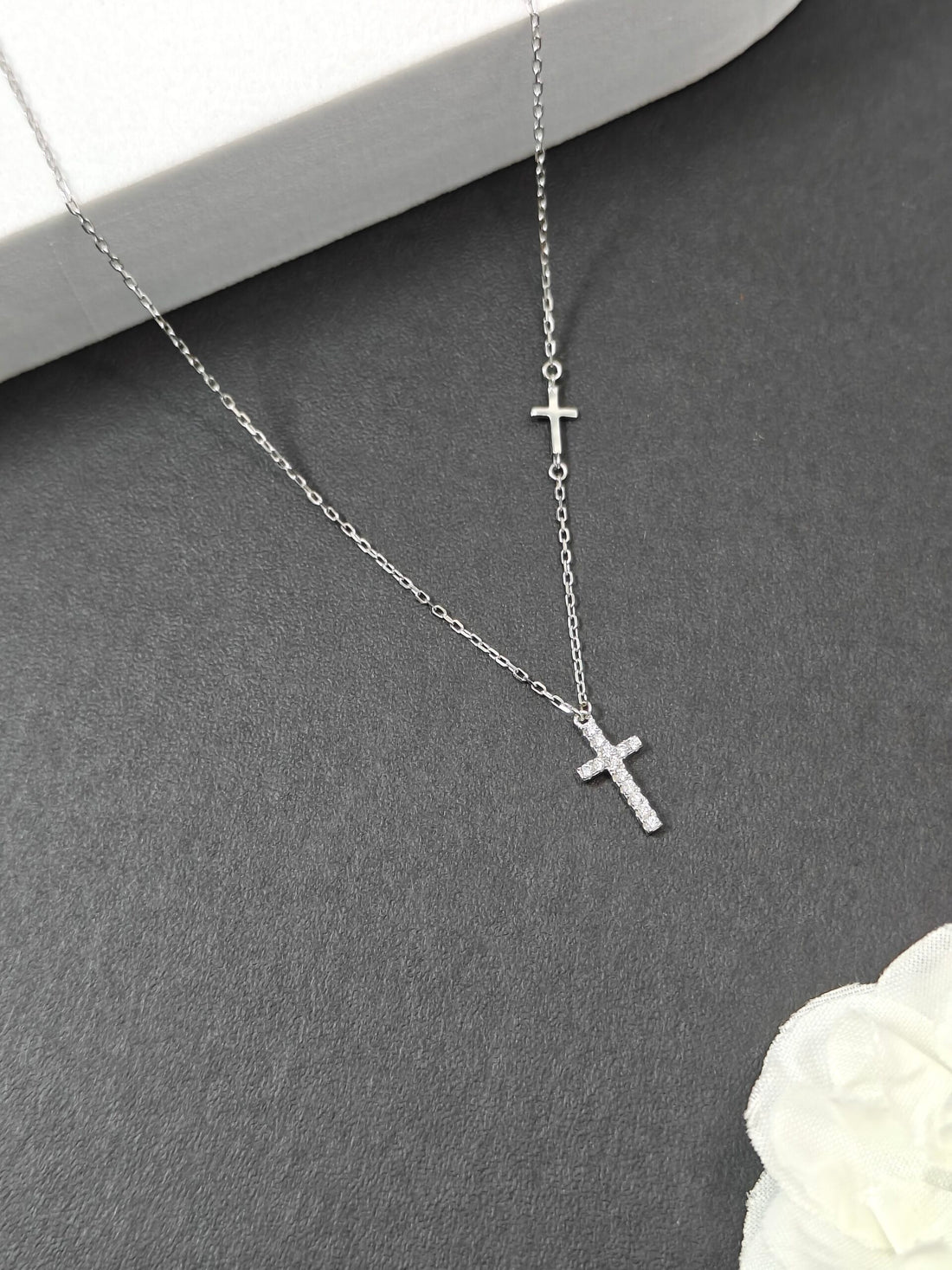 Silver cross necklace on a gray surface with a white flower