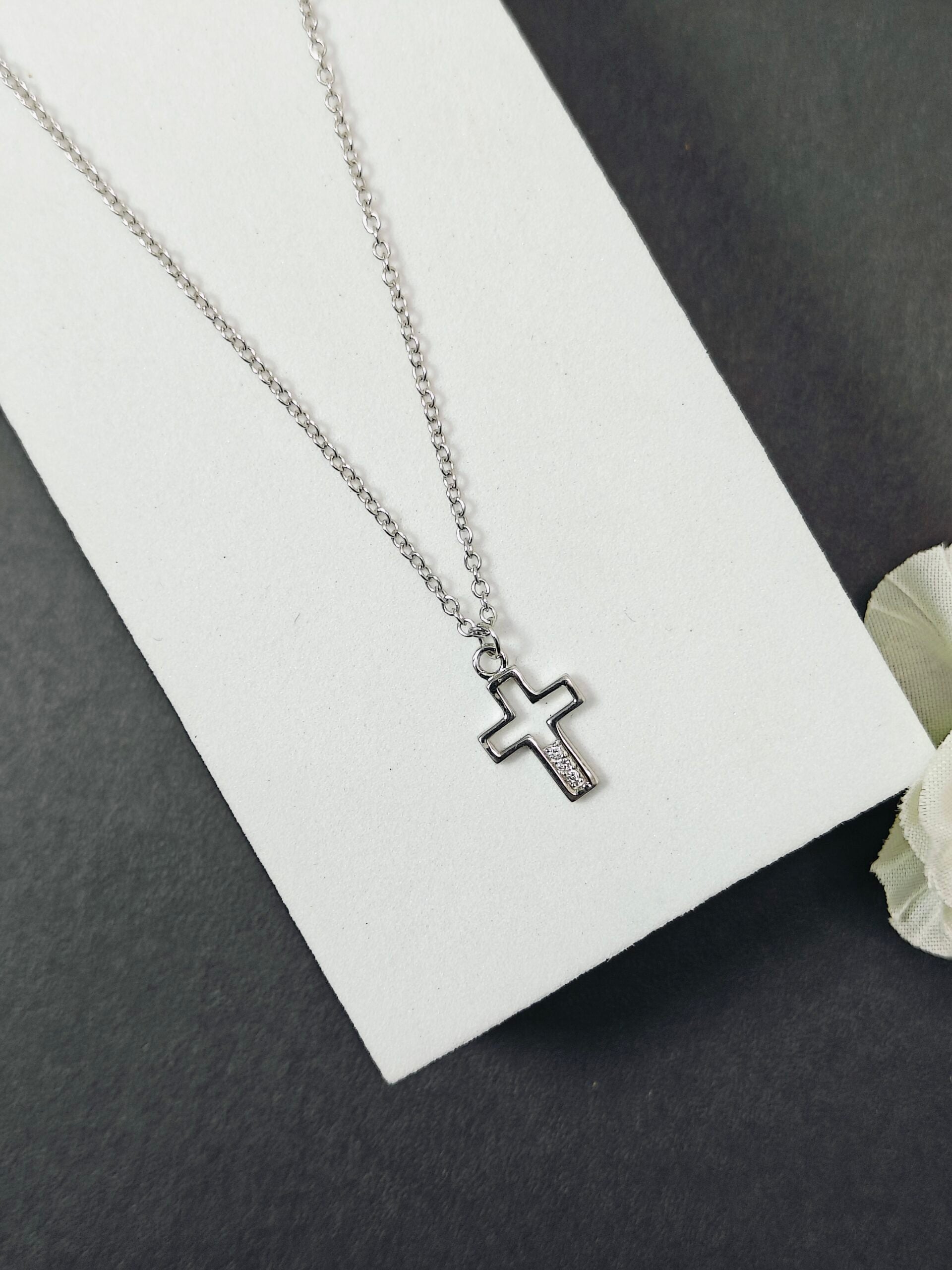 Silver cross necklace on a white card with a gray background