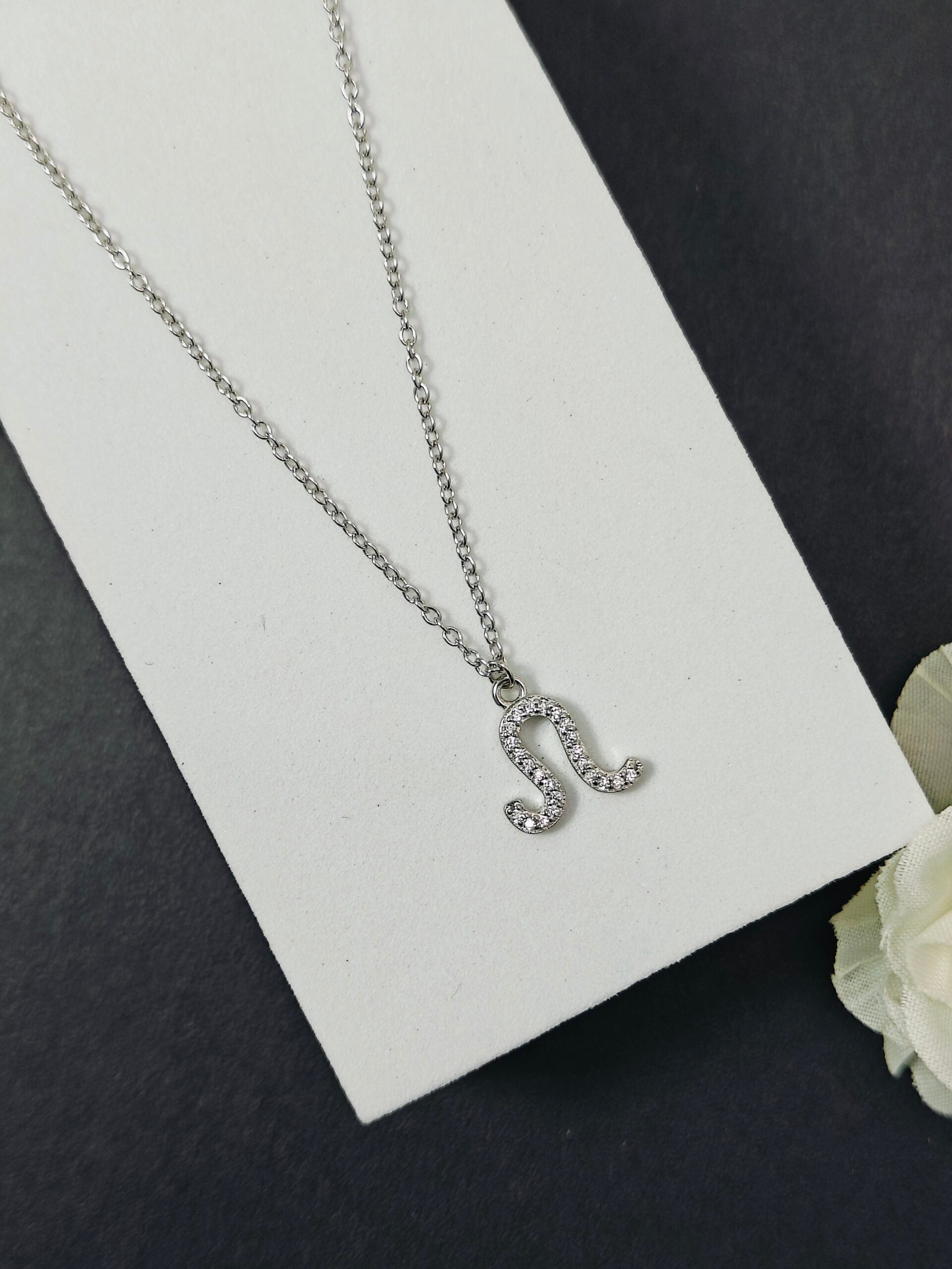 Silver necklace with a letter 'L' pendant on a white card with a black background