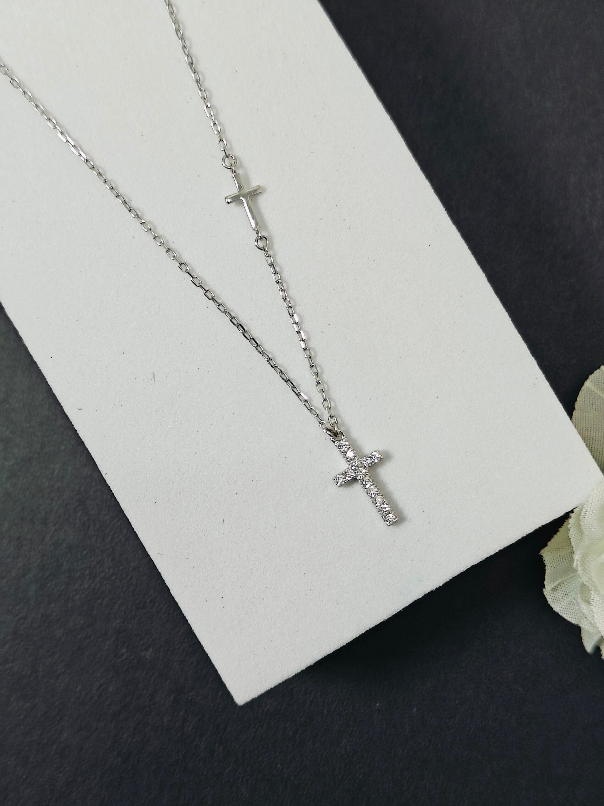 Silver cross necklace on a white card with a black background
