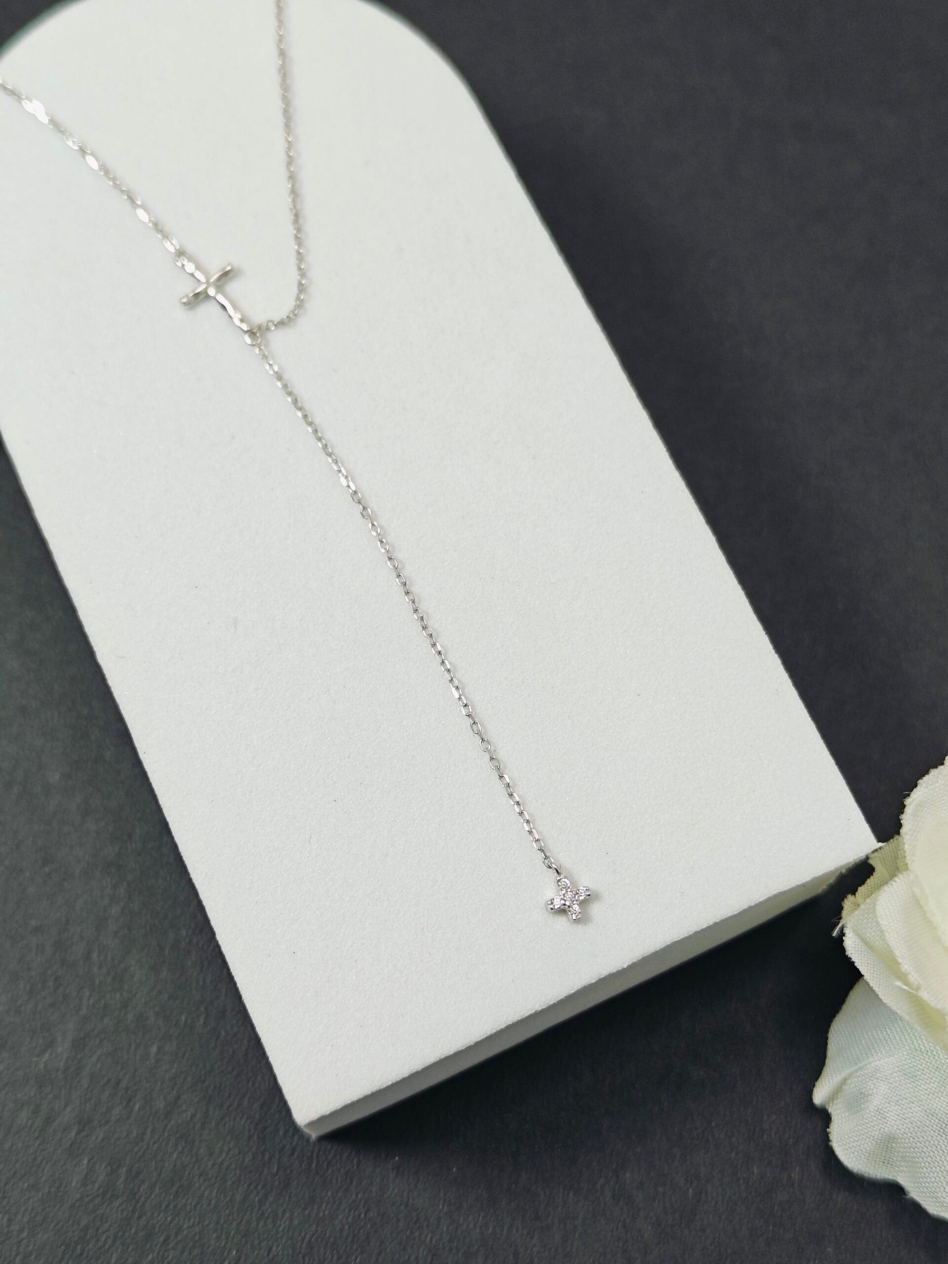 Silver necklace with a small pendant on a white card against a dark background