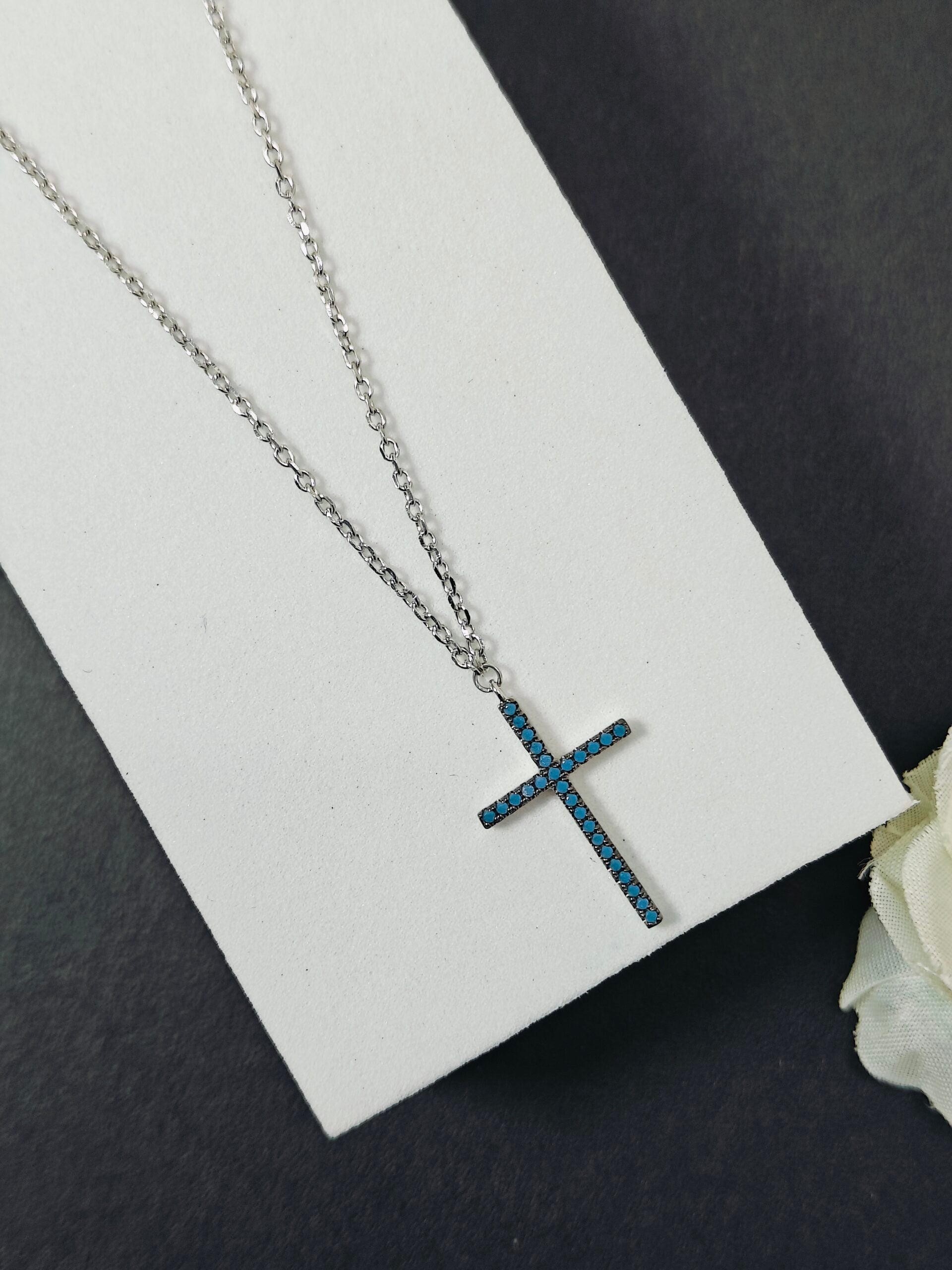 Silver cross necklace with blue stones on a white card