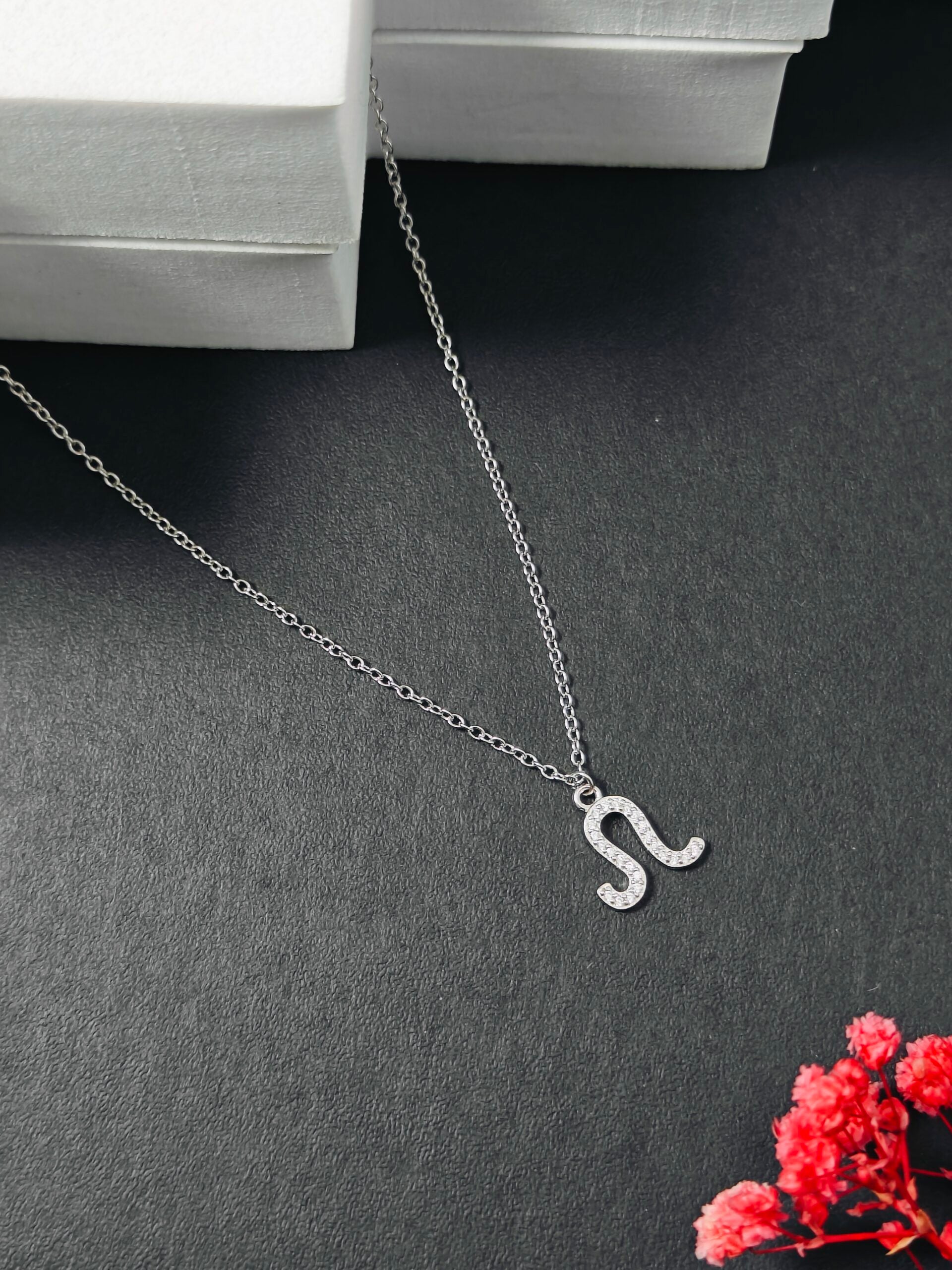 Silver necklace with a 'S' pendant on a dark surface with red flowers.