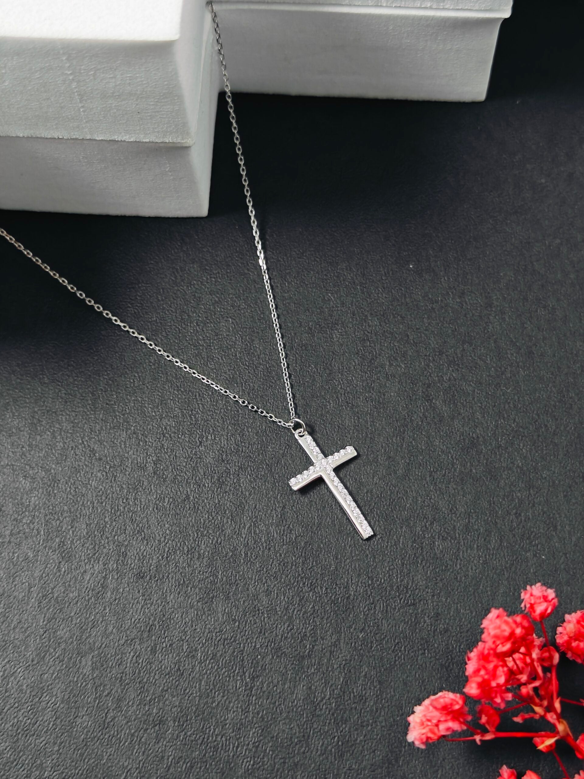 Silver cross necklace on a dark surface with red flowers