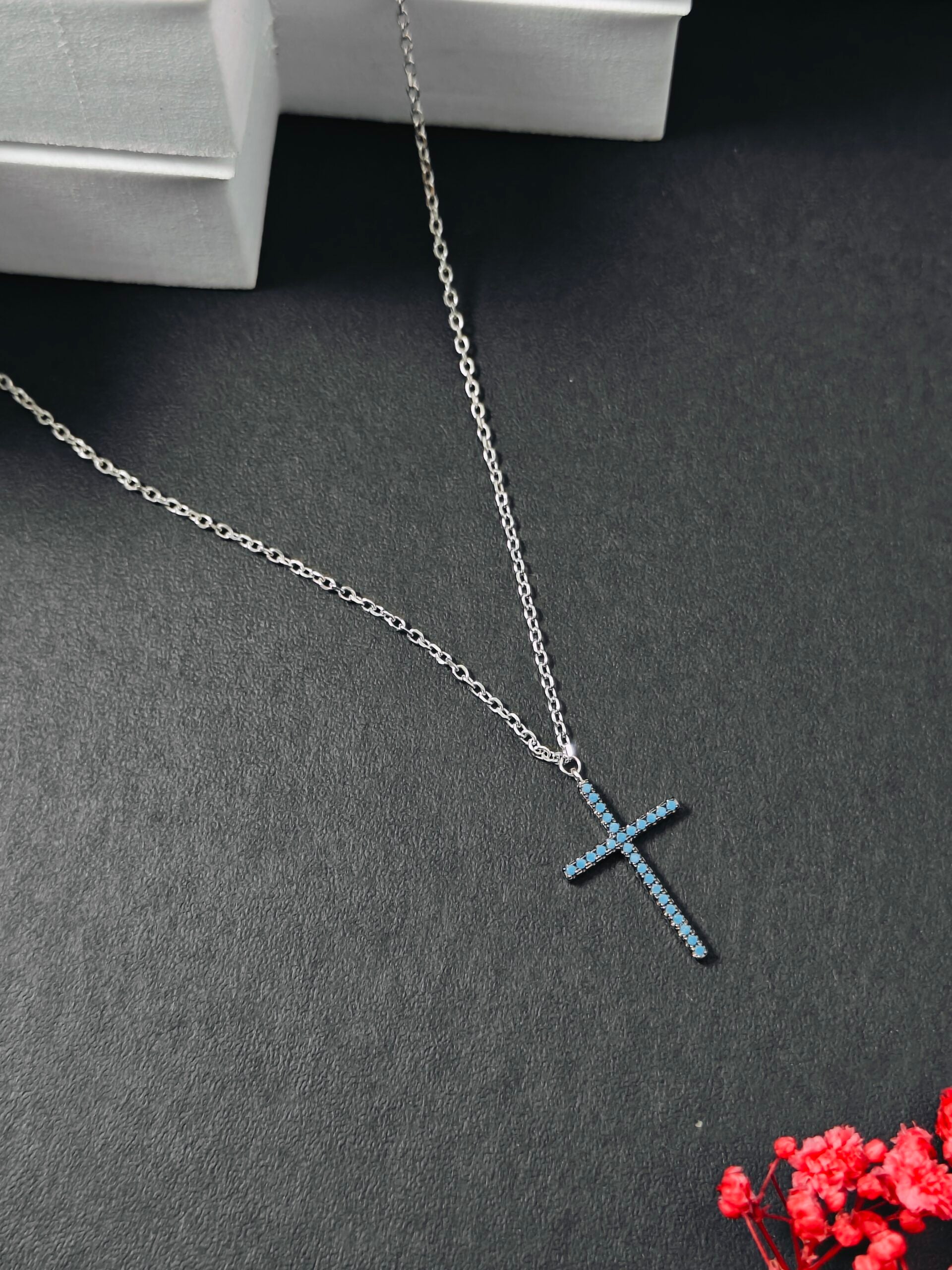 Silver necklace with a blue cross pendant on a dark surface