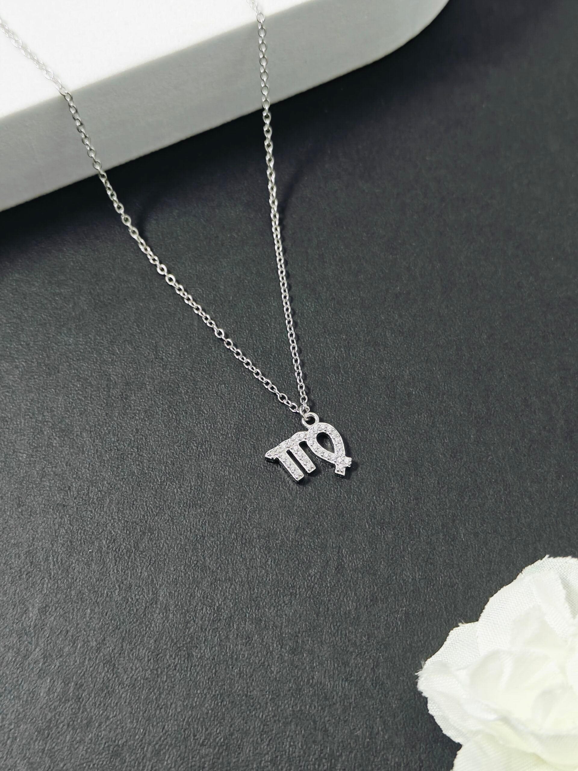 Silver necklace with 'TQ' pendant on a gray surface