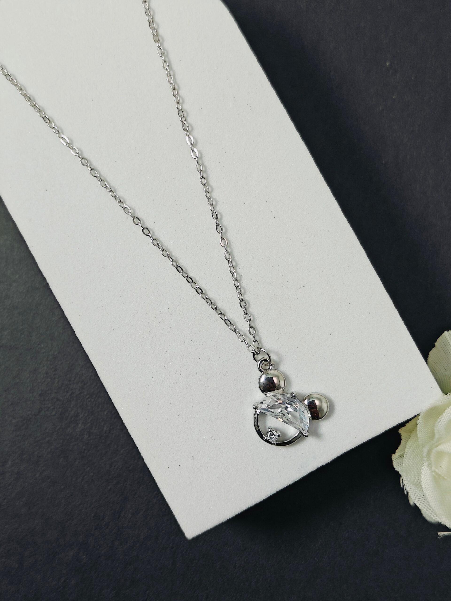 Silver necklace with a heart pendant on a white card against a dark background