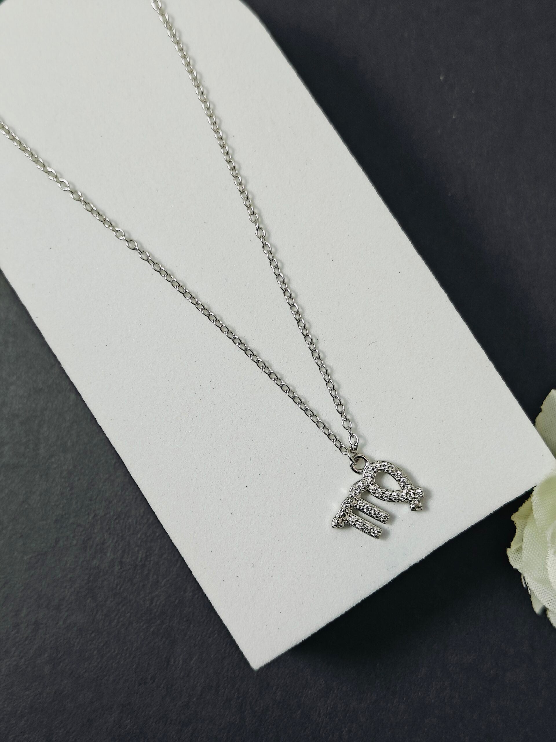 Silver necklace with a letter 'E' pendant on a white card against a dark background