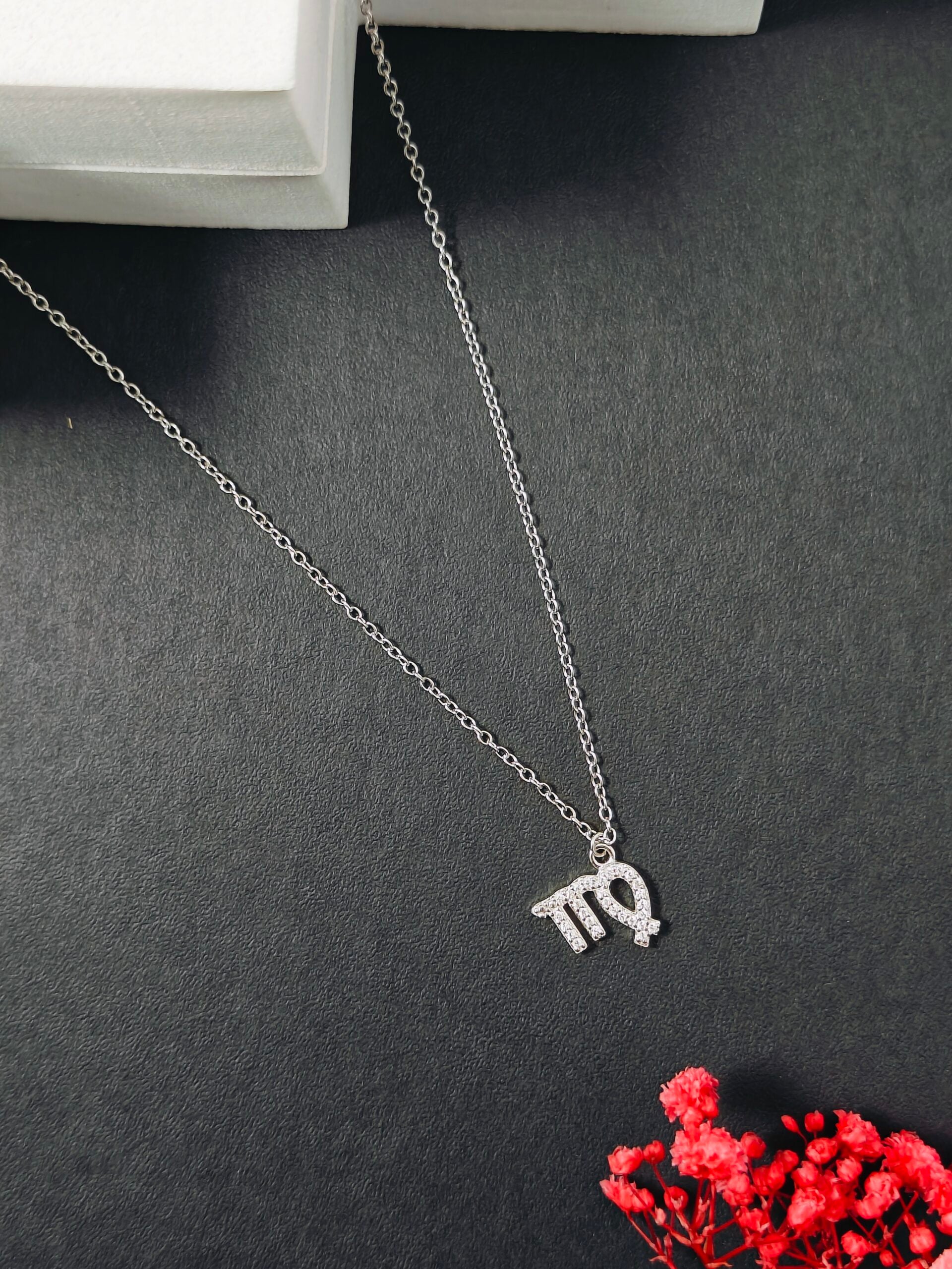 Silver necklace with a pendant on a dark surface with red flowers