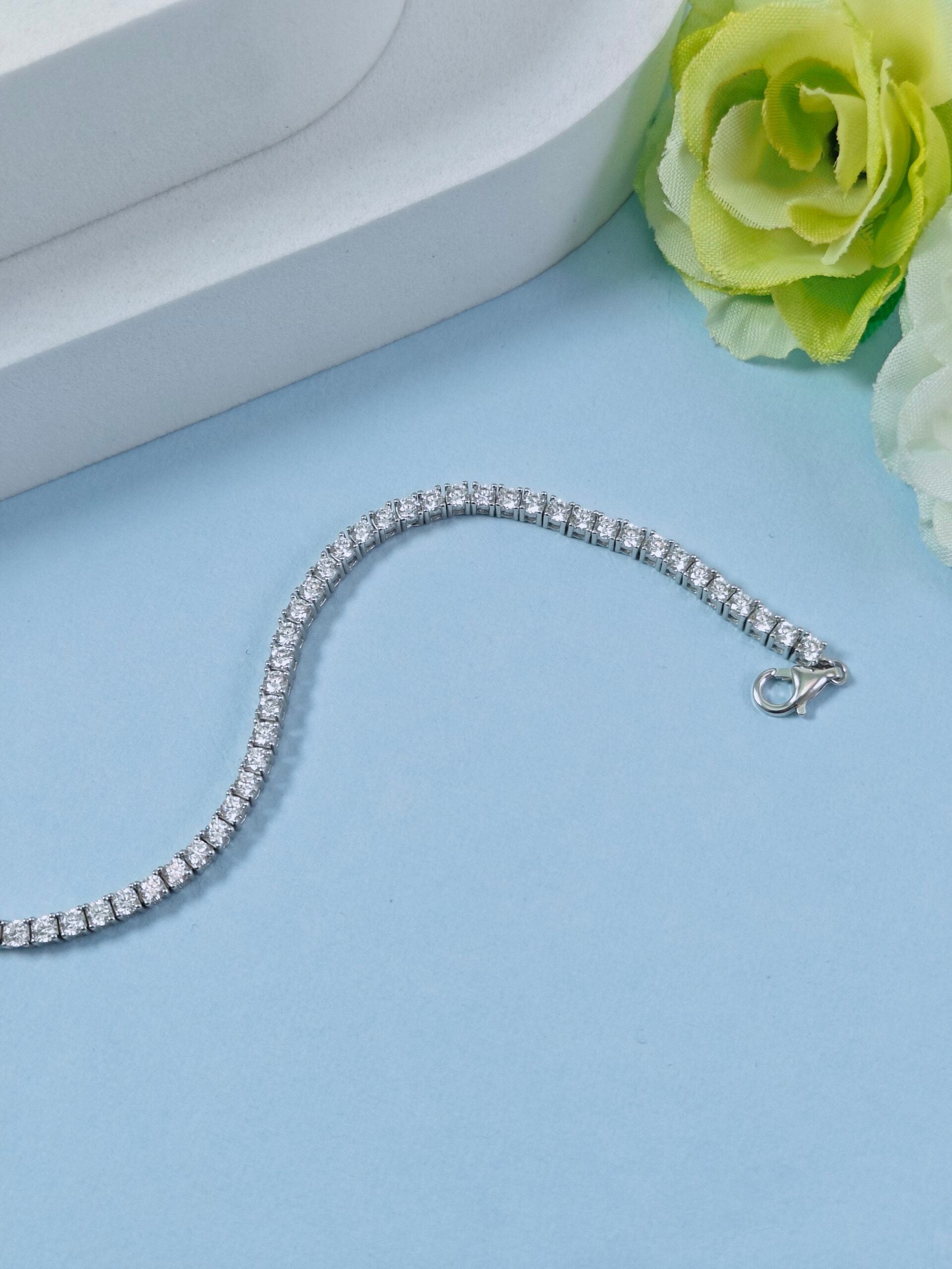 Silver bracelet on a light blue surface with a green rose.