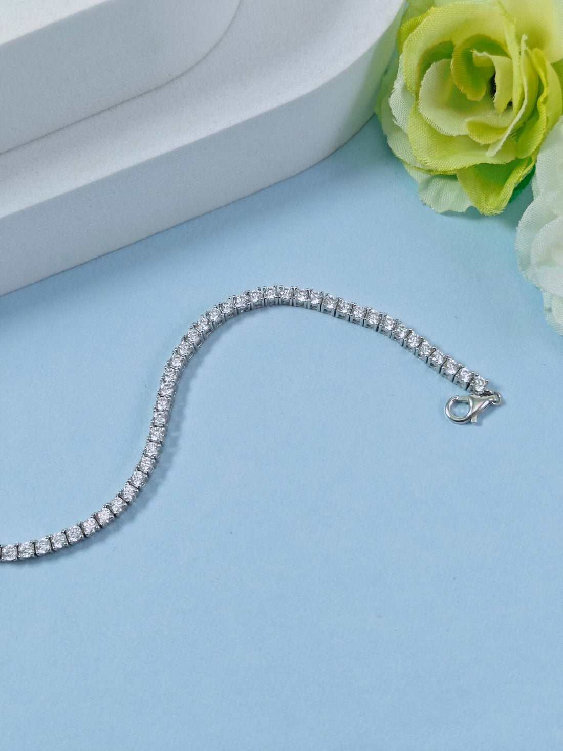 Silver bracelet on a light blue surface with a green rose.