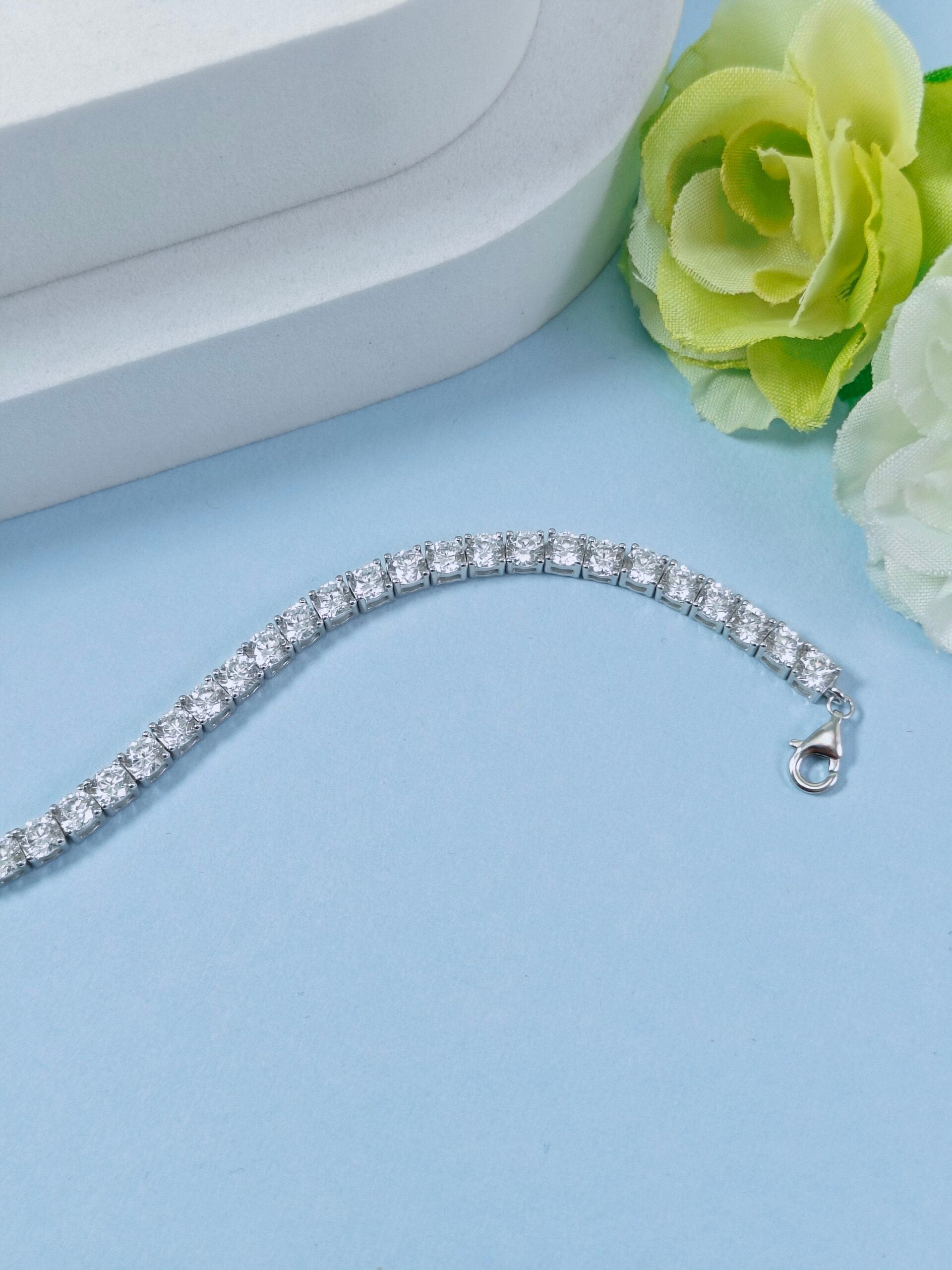 Silver bracelet on a light blue surface with a white and green flower in the background