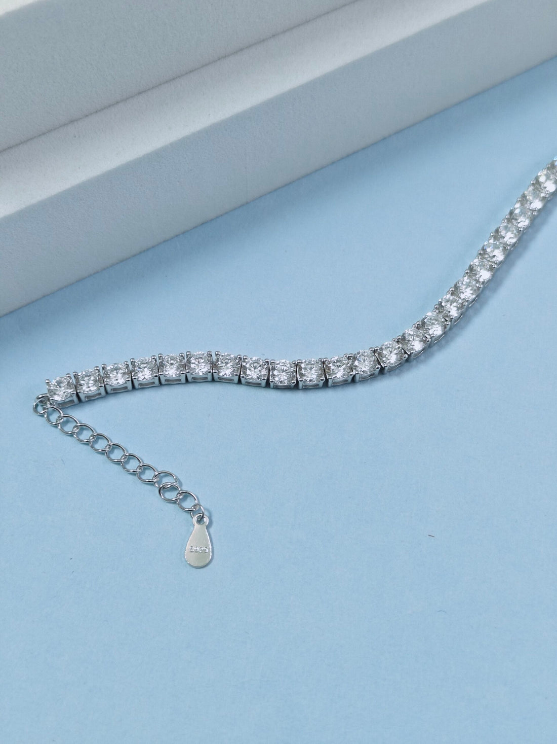 Silver bracelet with clear stones on a light blue background