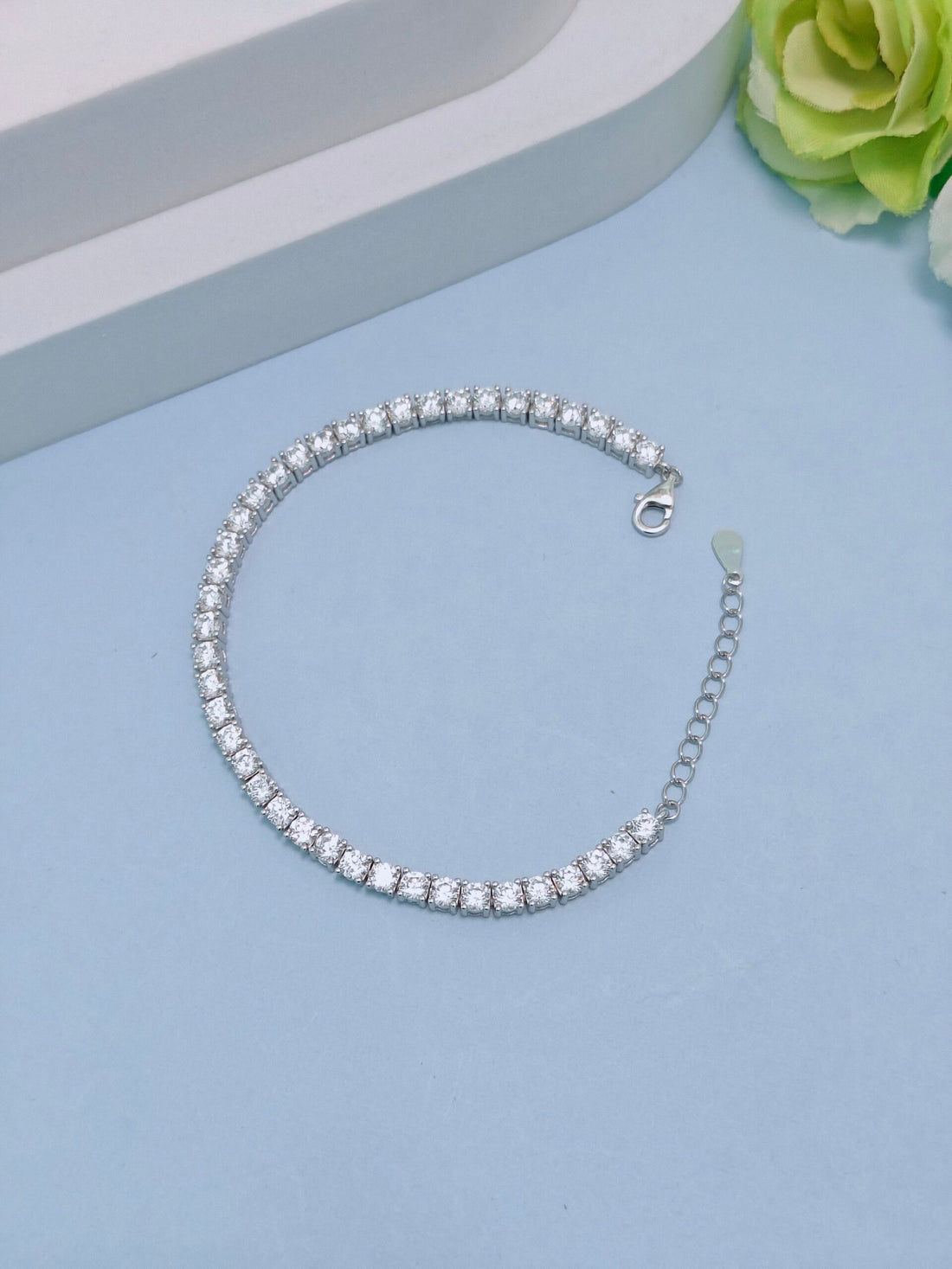 Silver bracelet with clear stones on a light blue surface with a green flower.