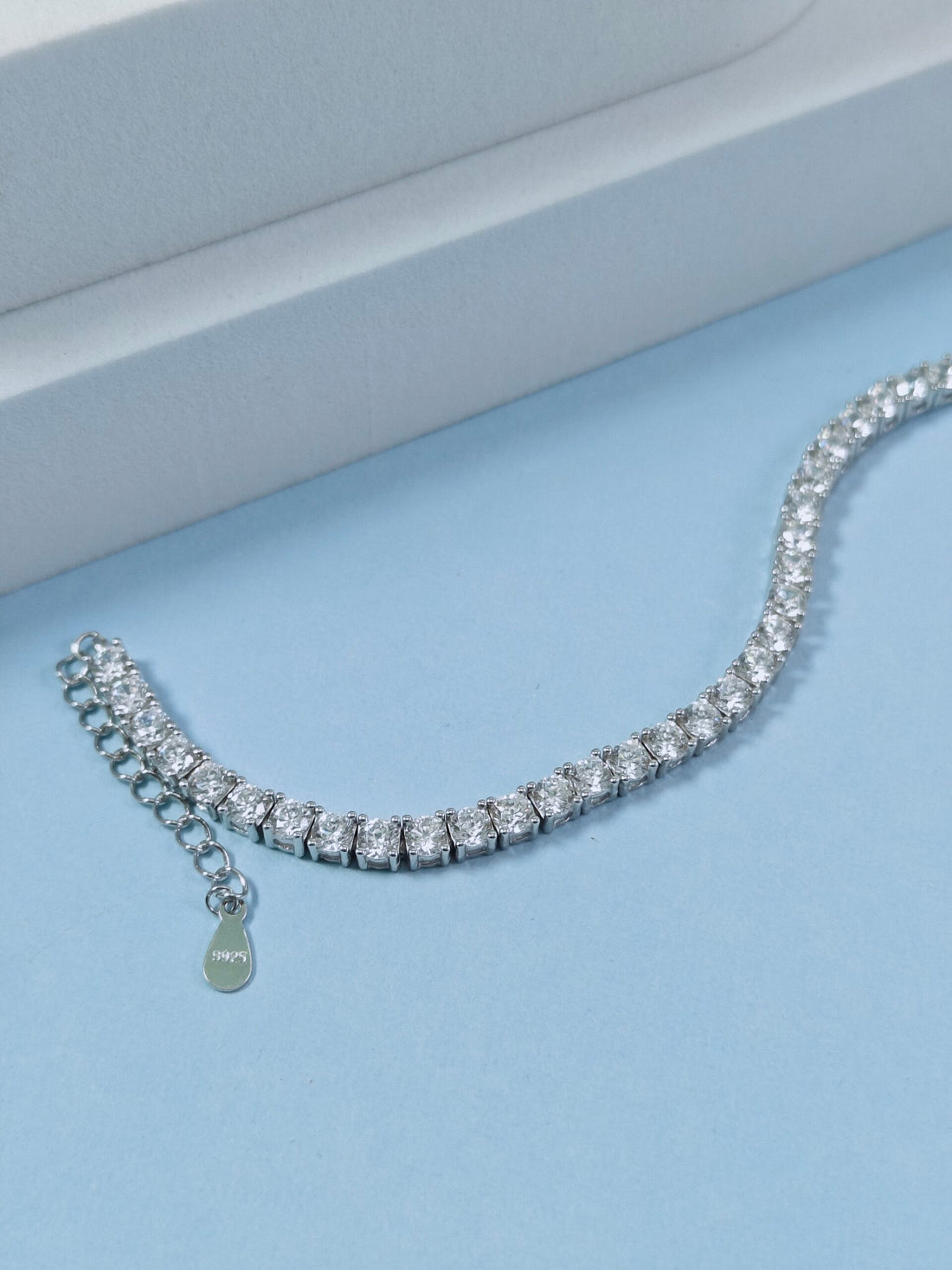 Silver bracelet with a teardrop charm on a light blue surface