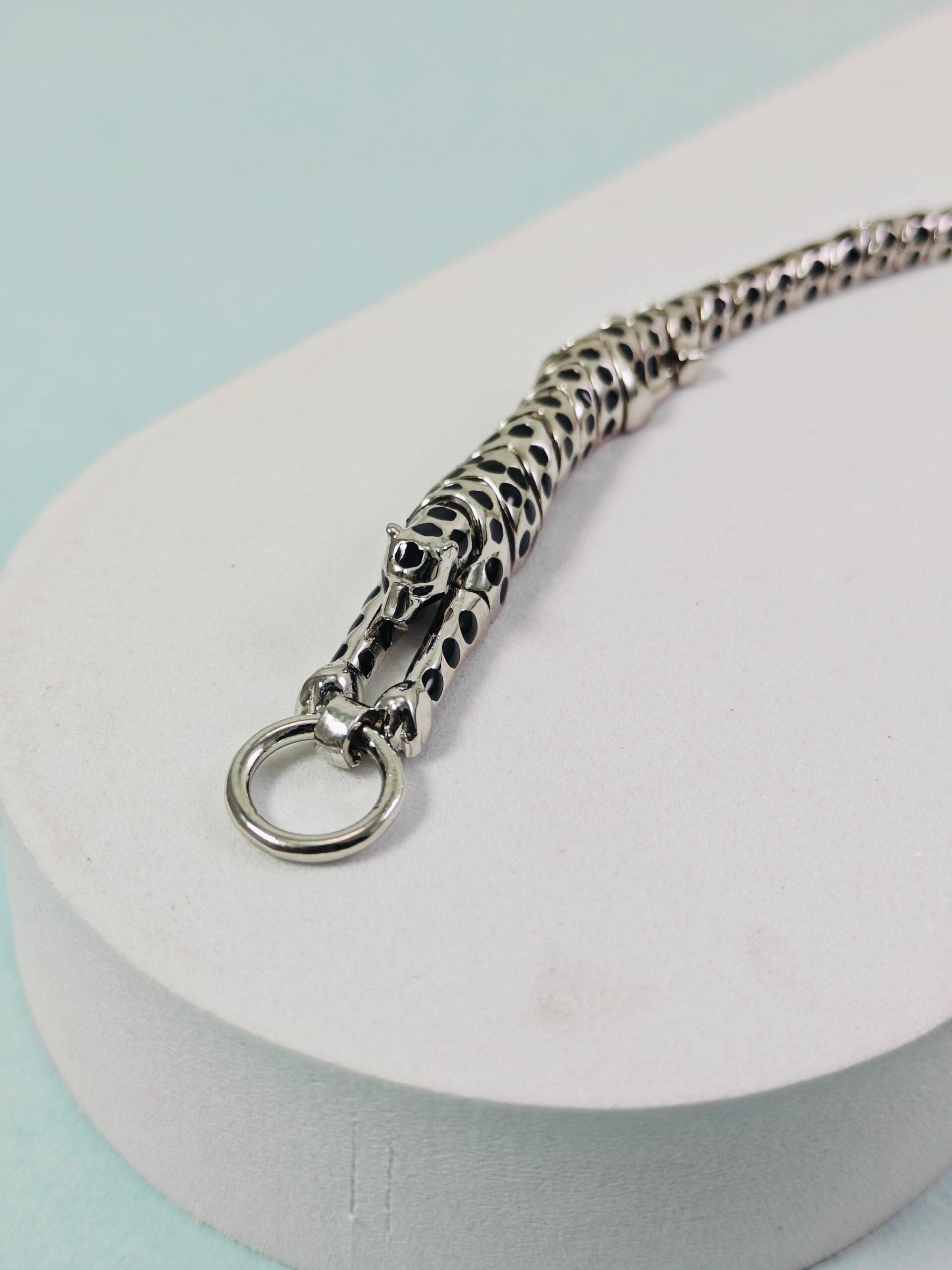 Silver chain necklace on a white stand with a light blue background
