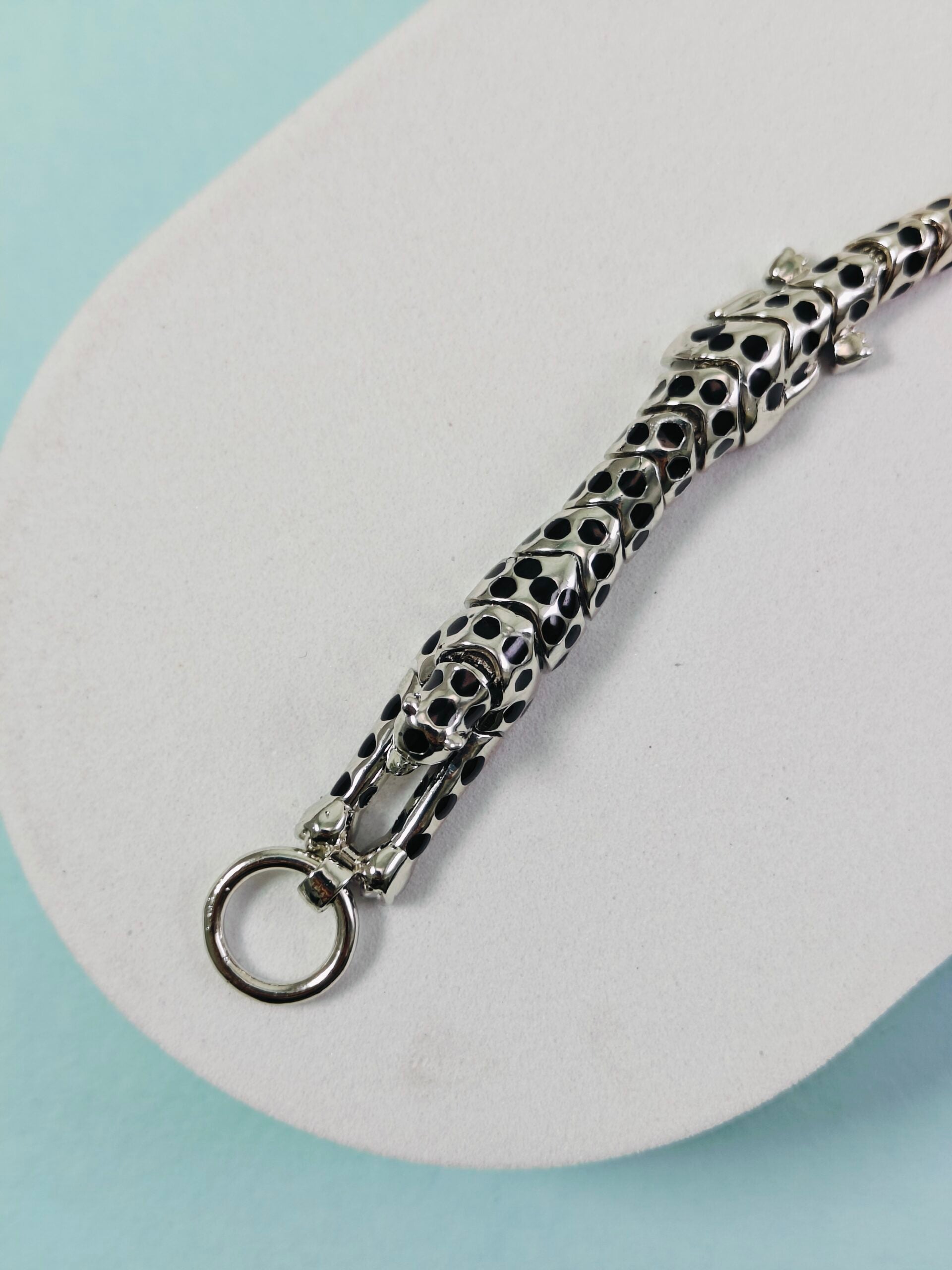 Silver chain with a unique design on a white platform against a light blue background