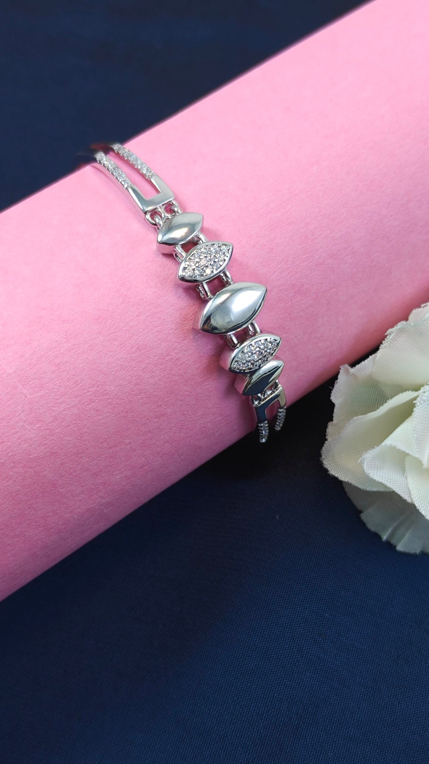 Silver bracelet with leaf-shaped charms on a pink surface with a white flower.