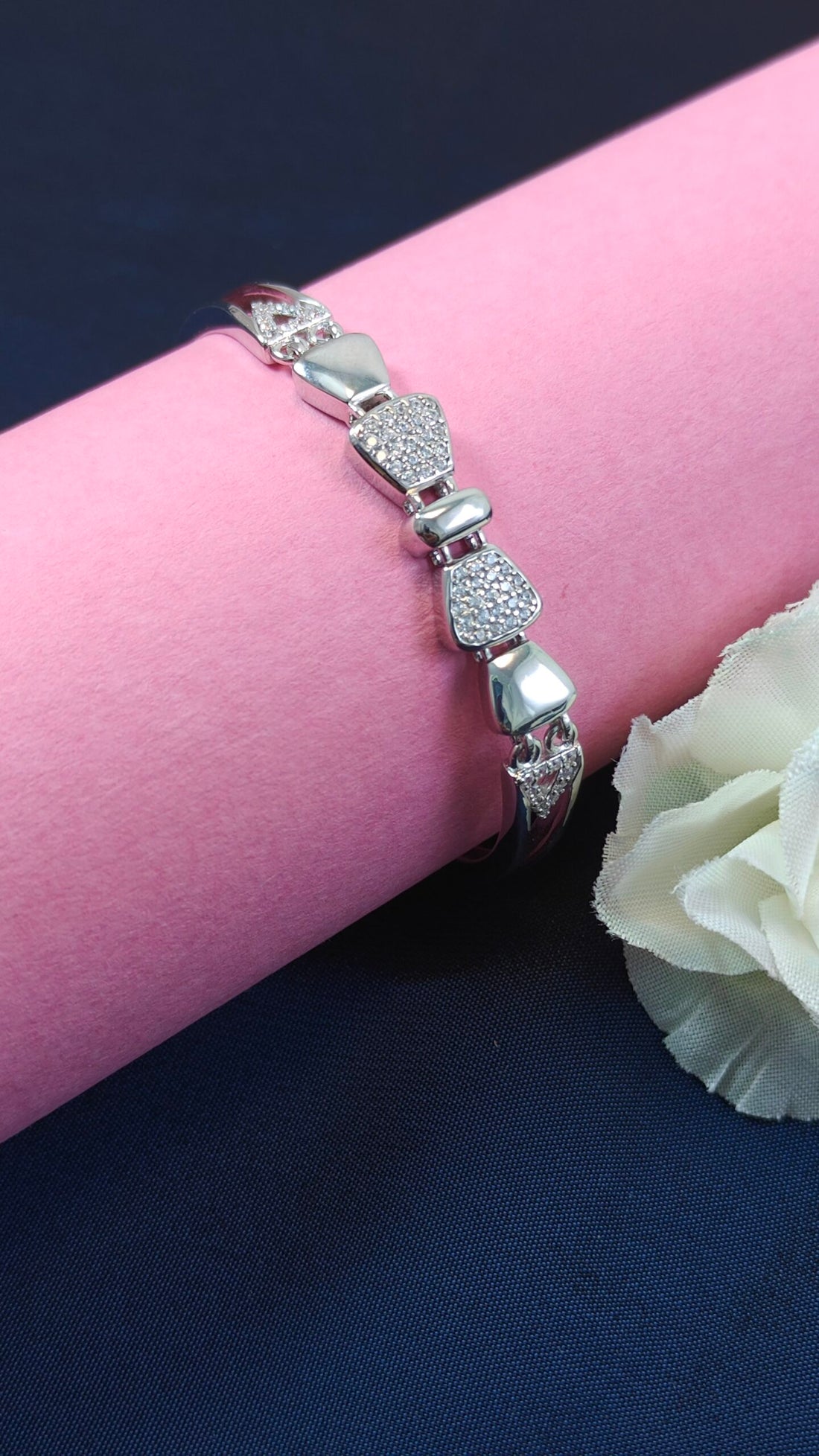Silver bracelet with heart-shaped charms on a wrist against a pink and blue background