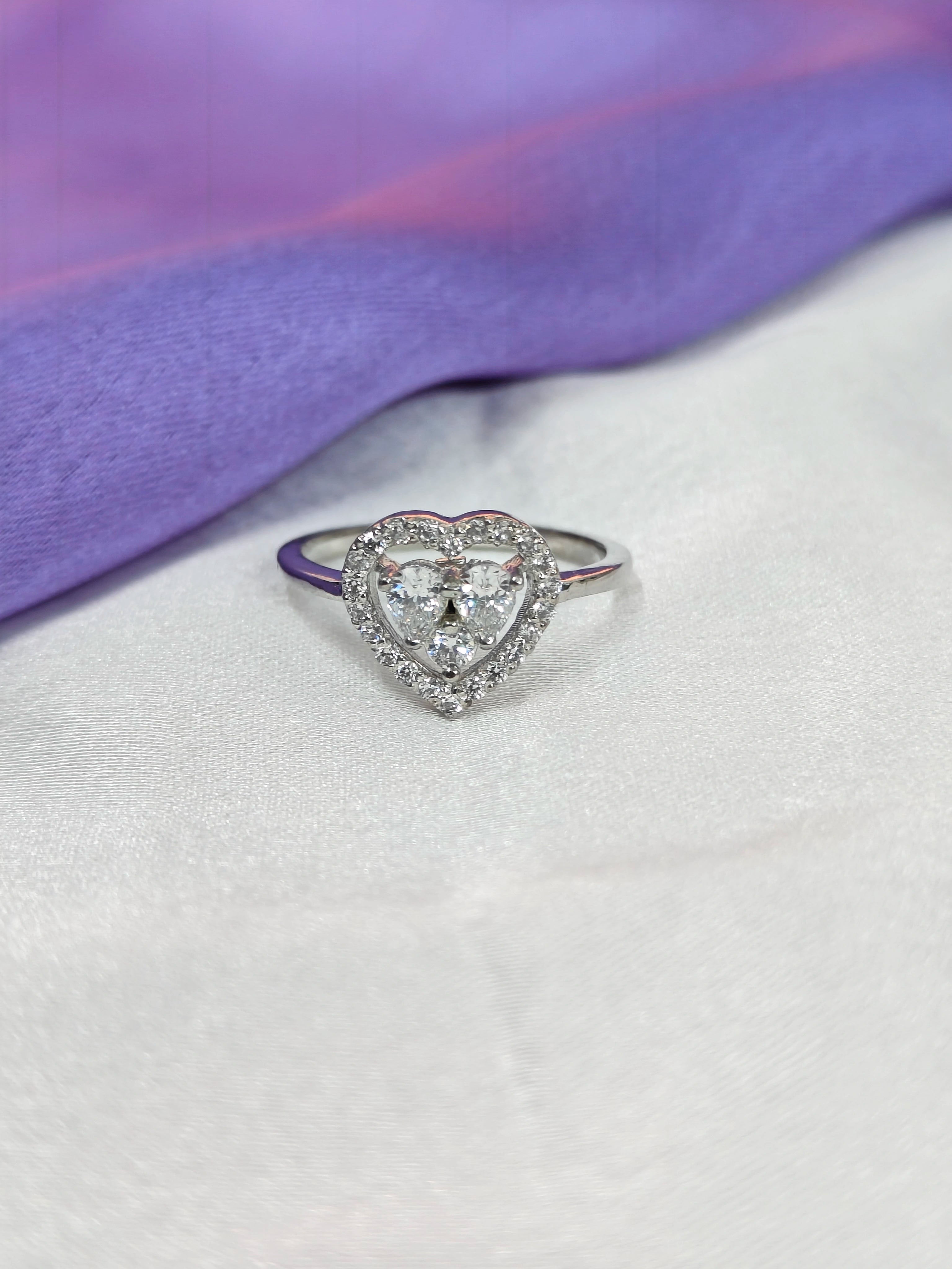 Heart-shaped diamond ring on a white surface with a purple fabric background