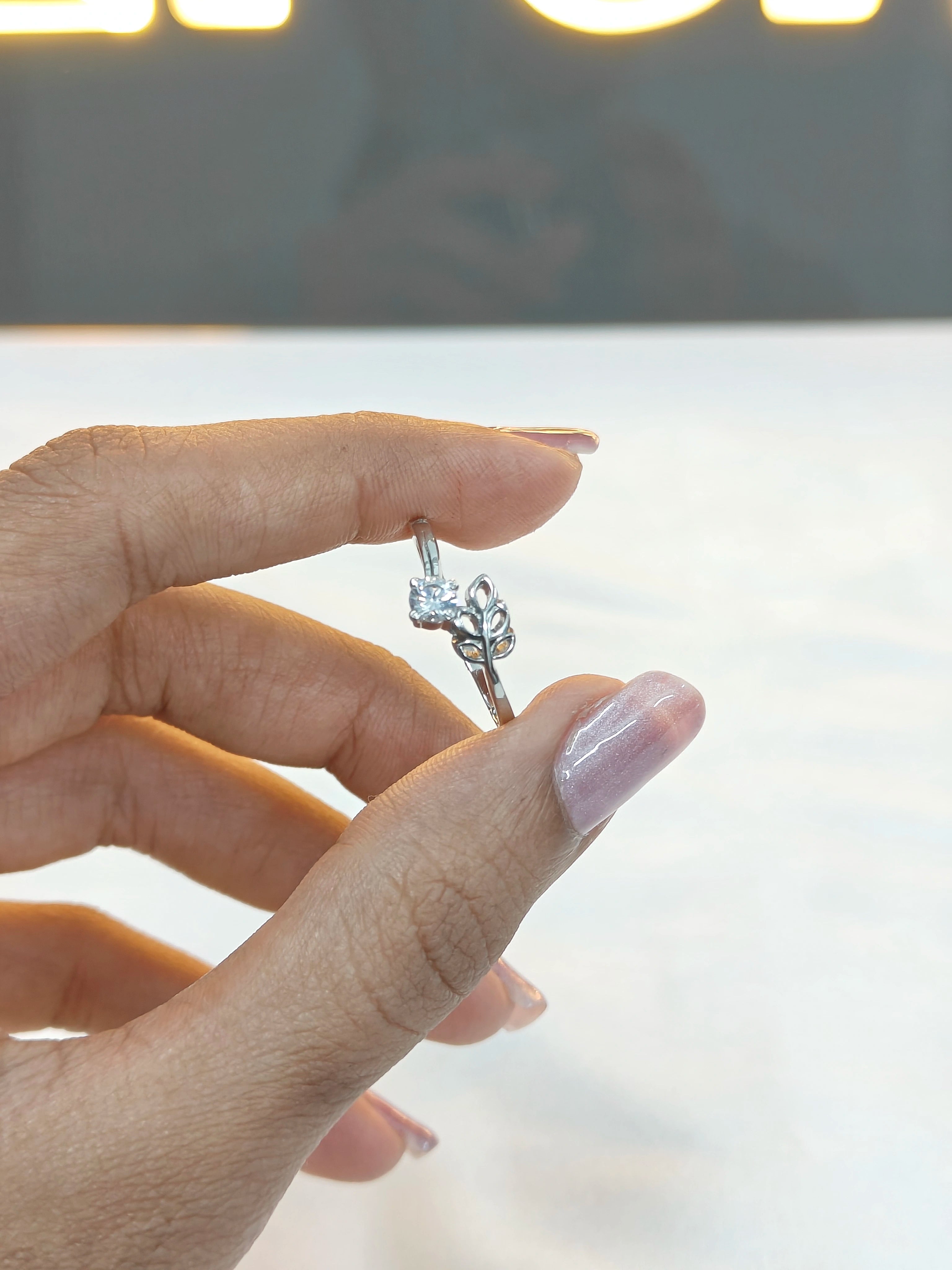 Hand holding a silver ring with a clear stone against a blurred background