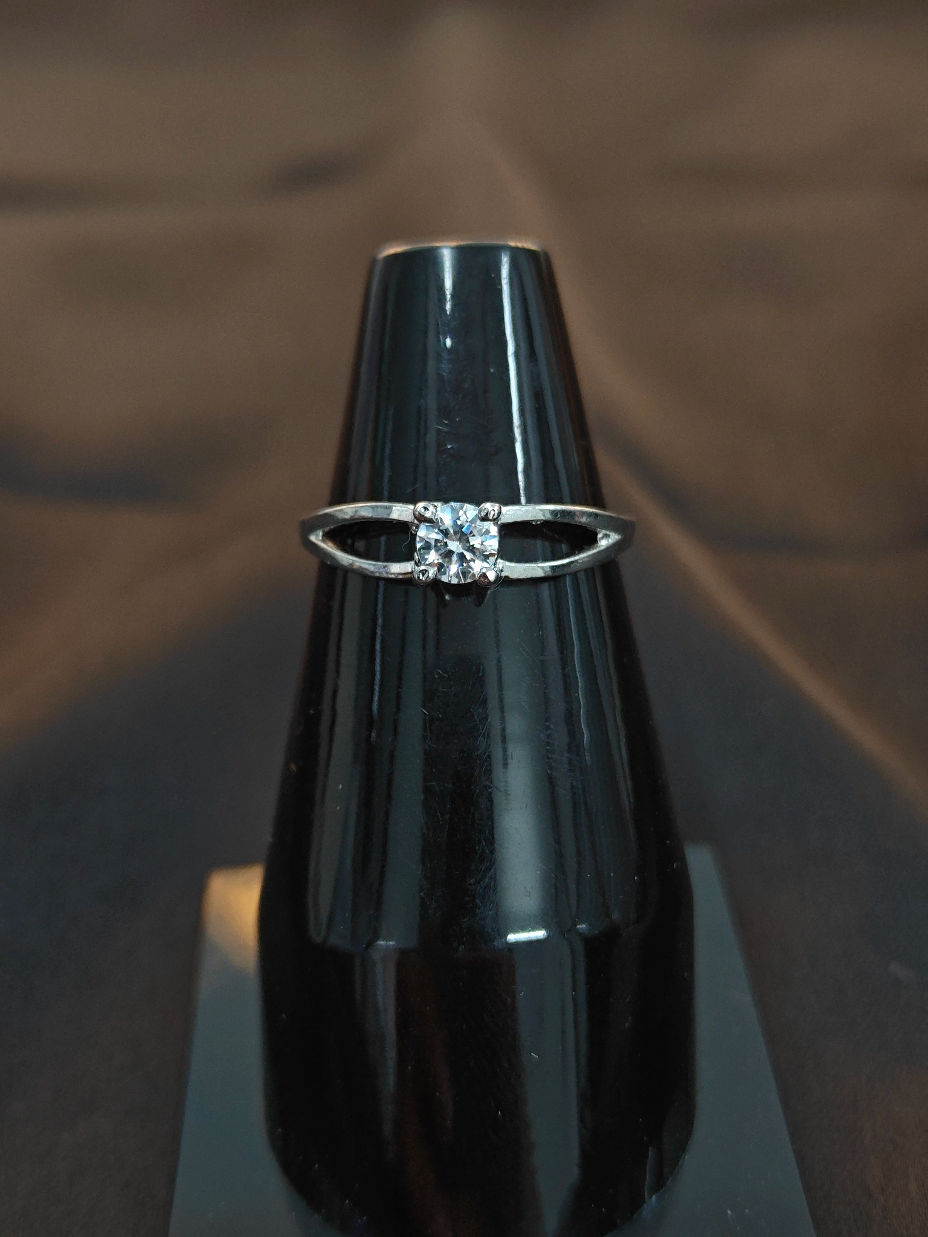 Silver ring with a diamond on a black stand against a dark background