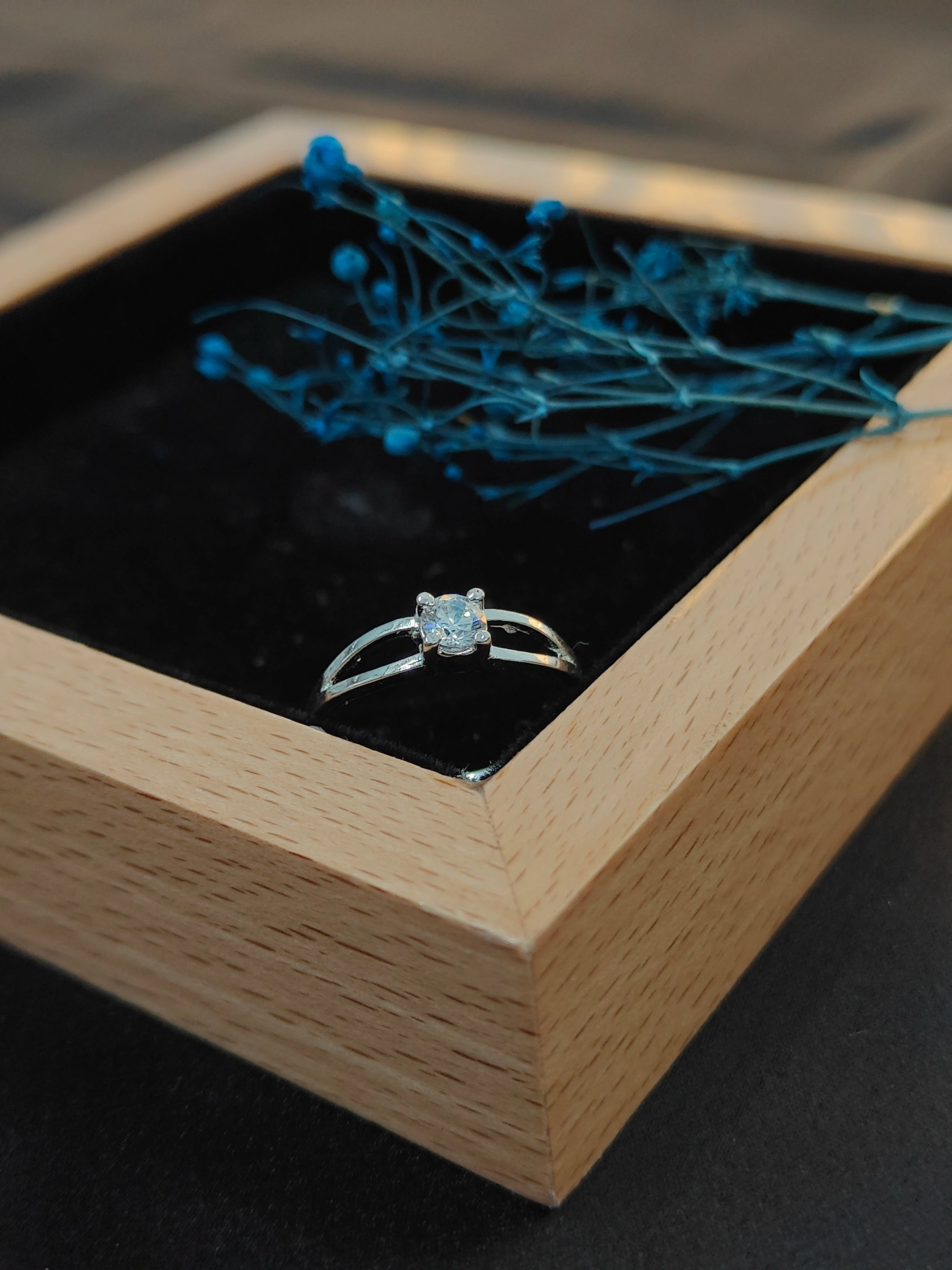 Diamond ring in a wooden box with decorative blue flowers on a dark background