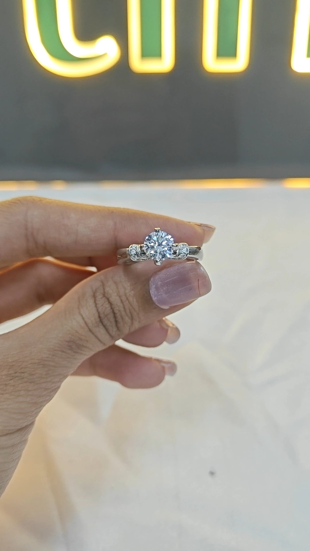 Hand holding a diamond ring with a blurred neon sign in the background