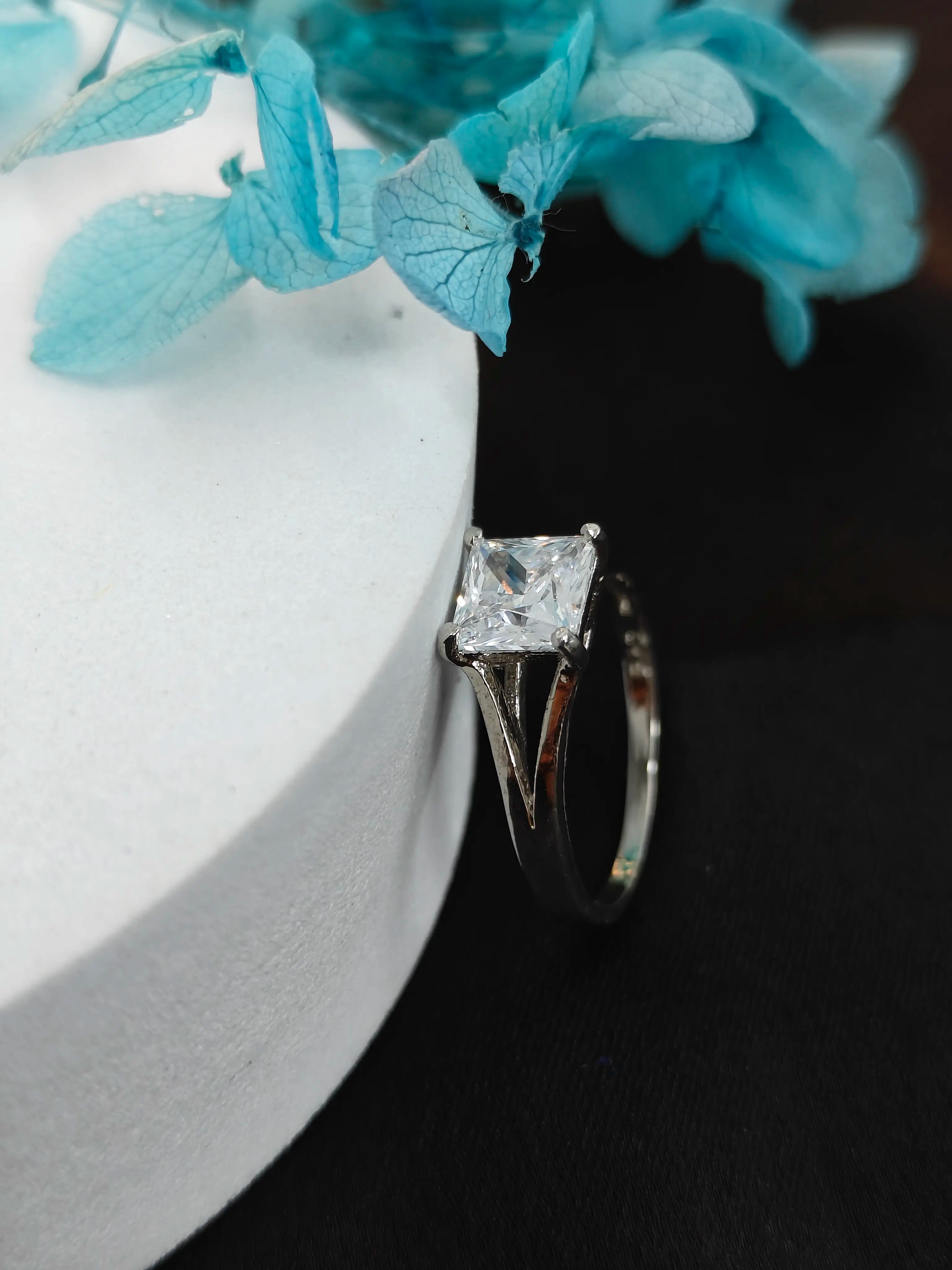 Diamond ring on a dark surface with light blue flowers in the background