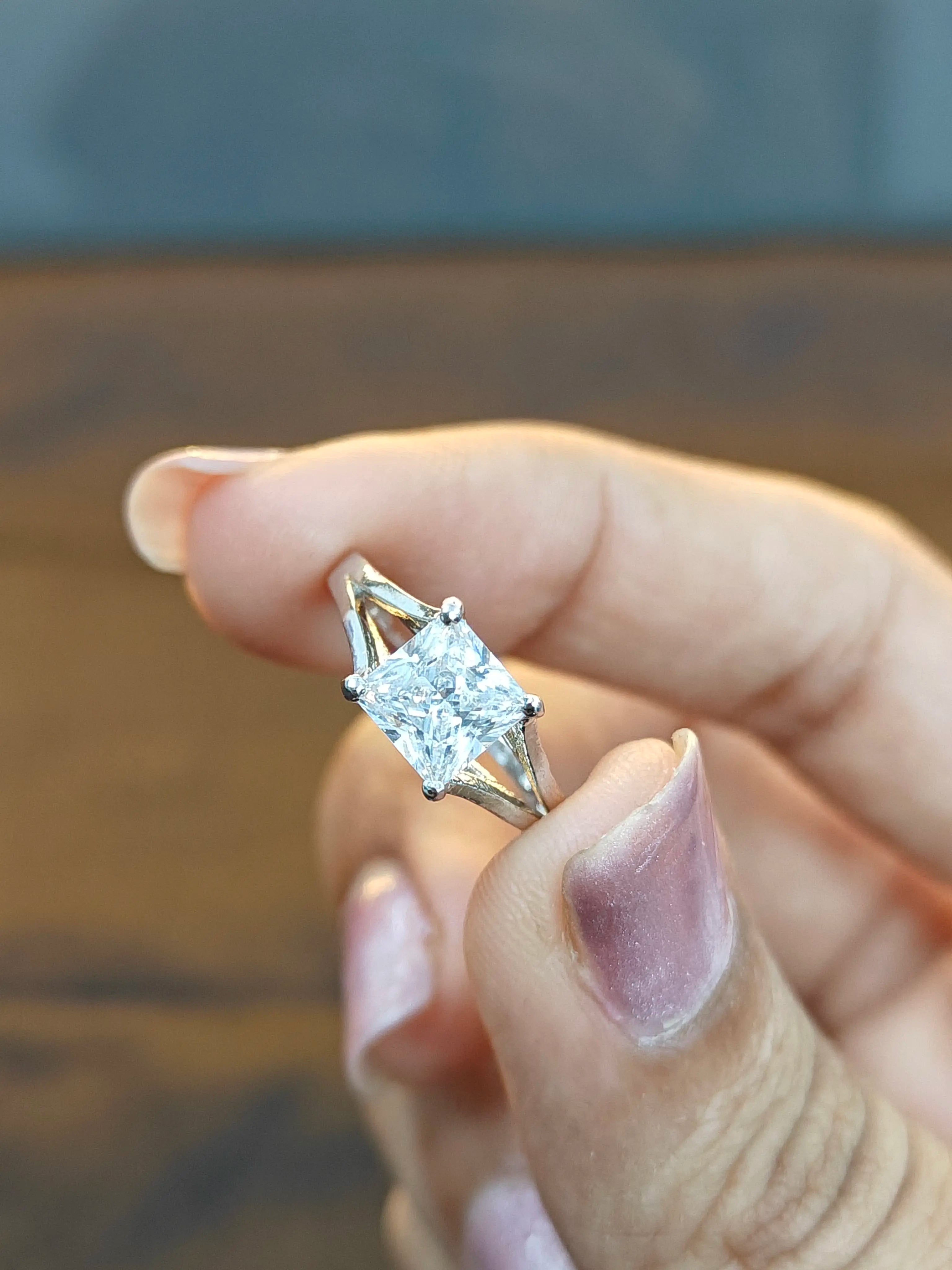 Gold ring with a diamond held between fingers against a blurred background