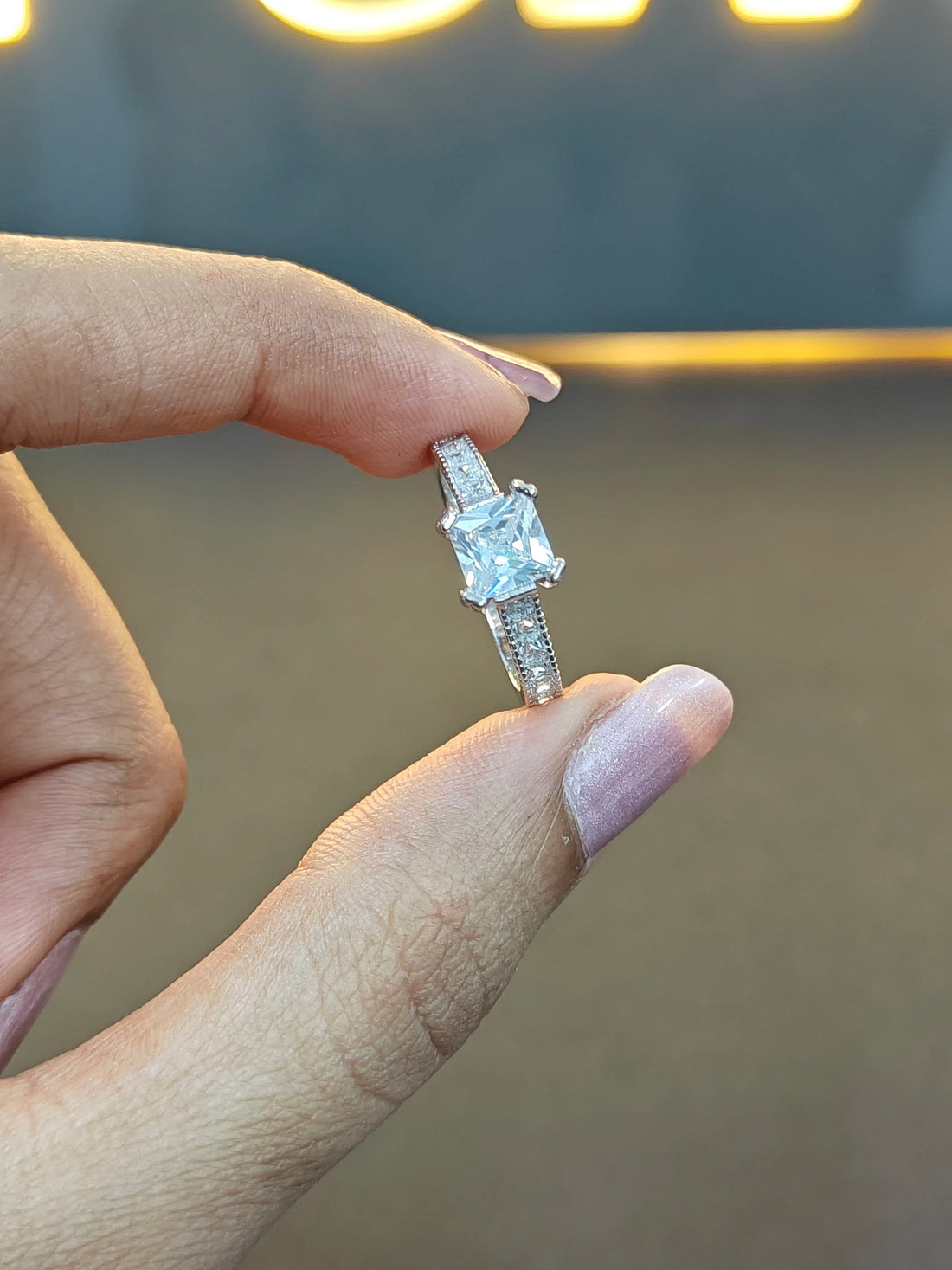 Diamond ring held between fingers against a neutral background