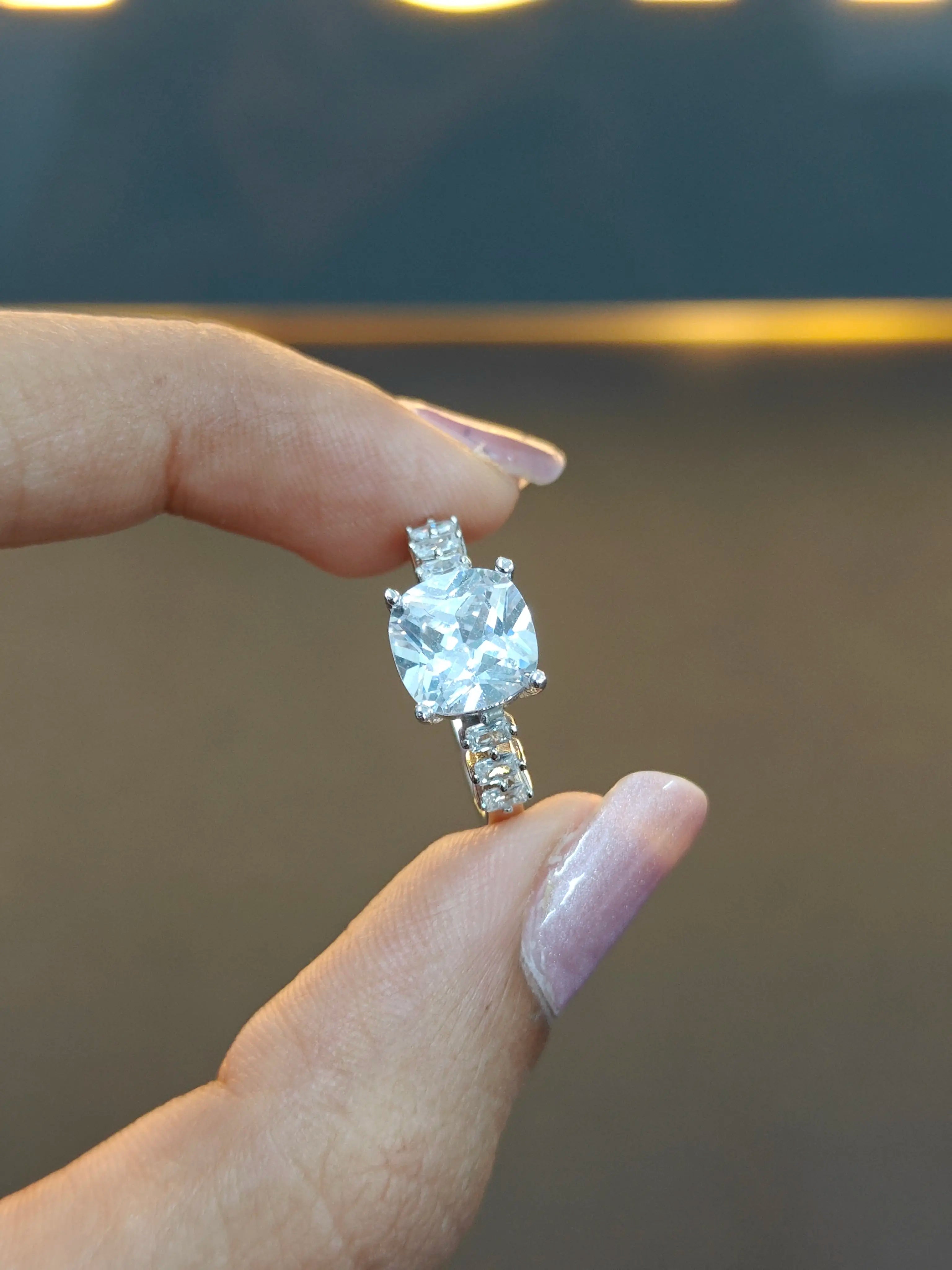 Diamond ring held between fingers against a blurred background