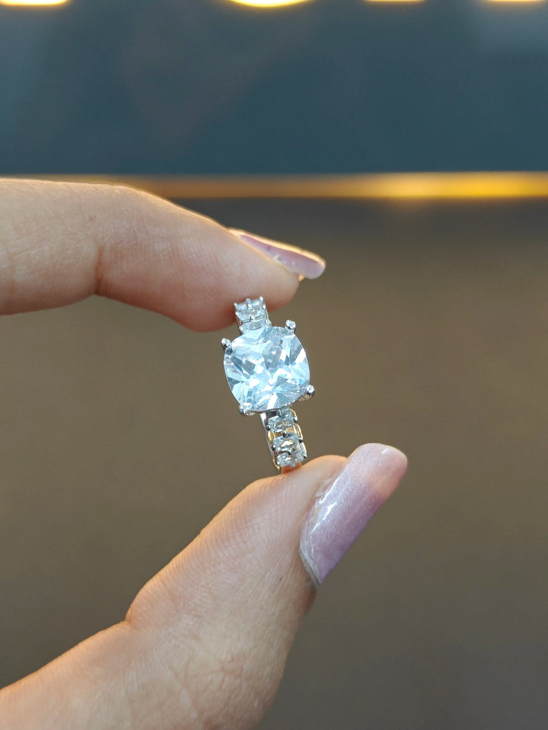 Diamond ring held between fingers against a blurred background