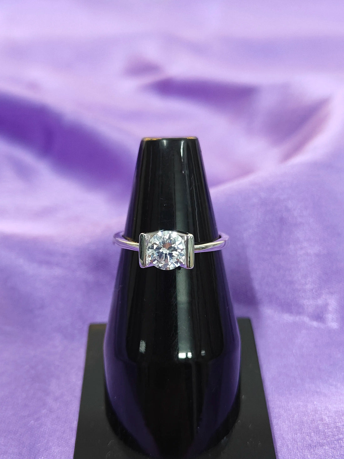 Diamond ring on a black stand against a purple fabric background