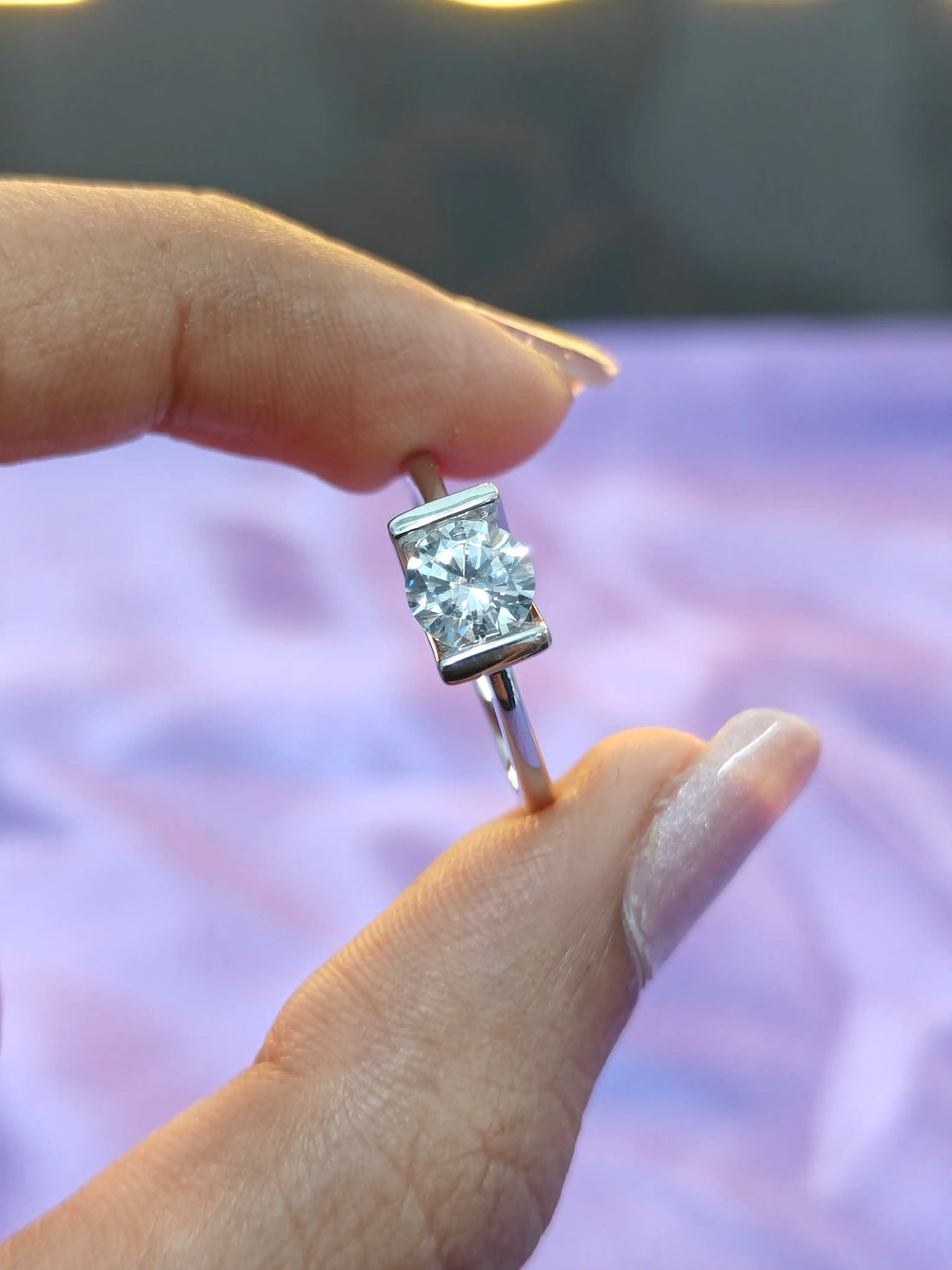 Silver earring with clear gemstone held between fingers against a blurred background