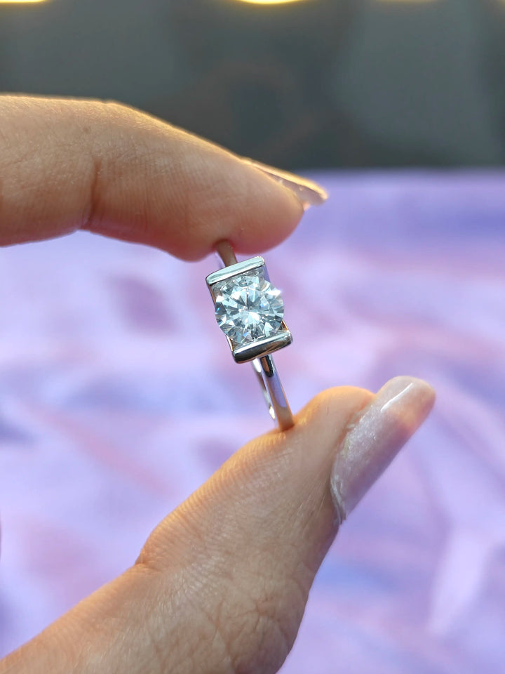 Silver earring with clear gemstone held between fingers against a blurred background