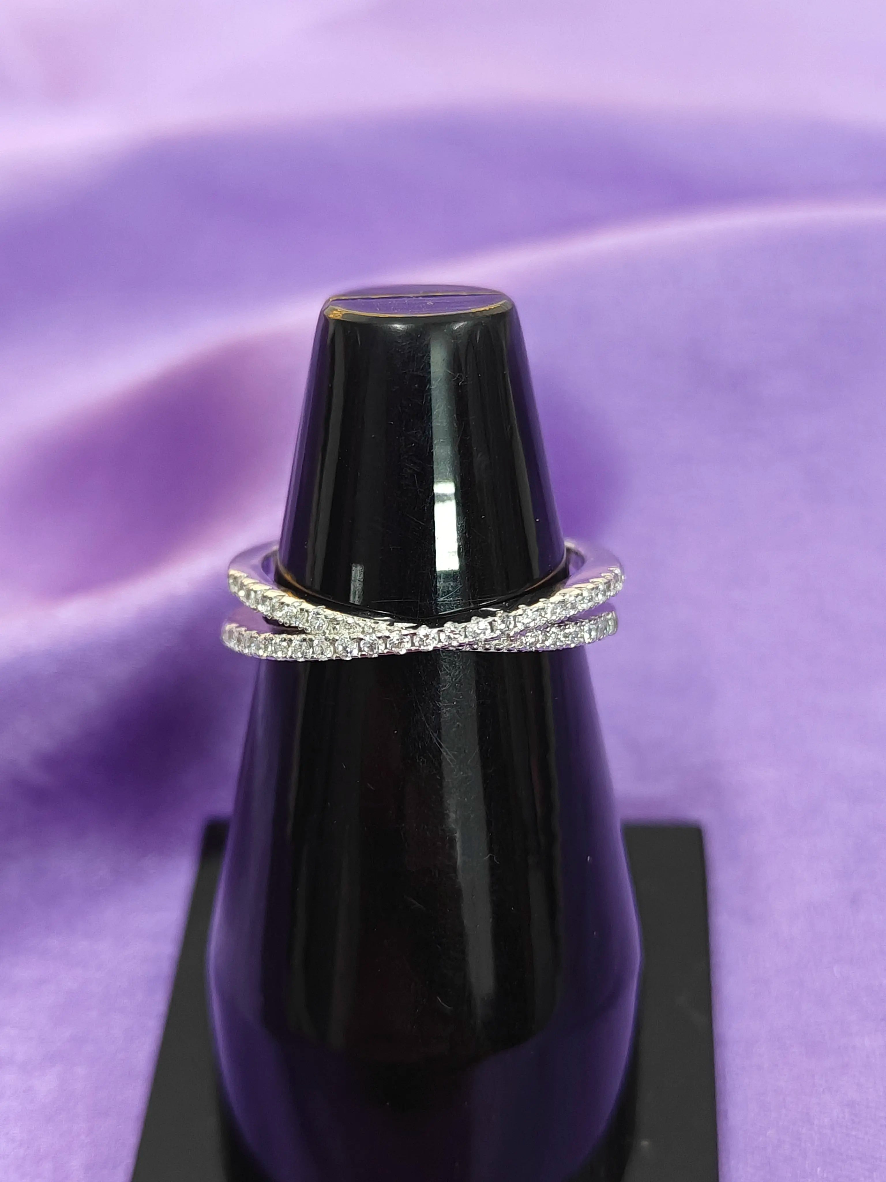 Silver ring with diamonds on a black stand against a purple fabric background