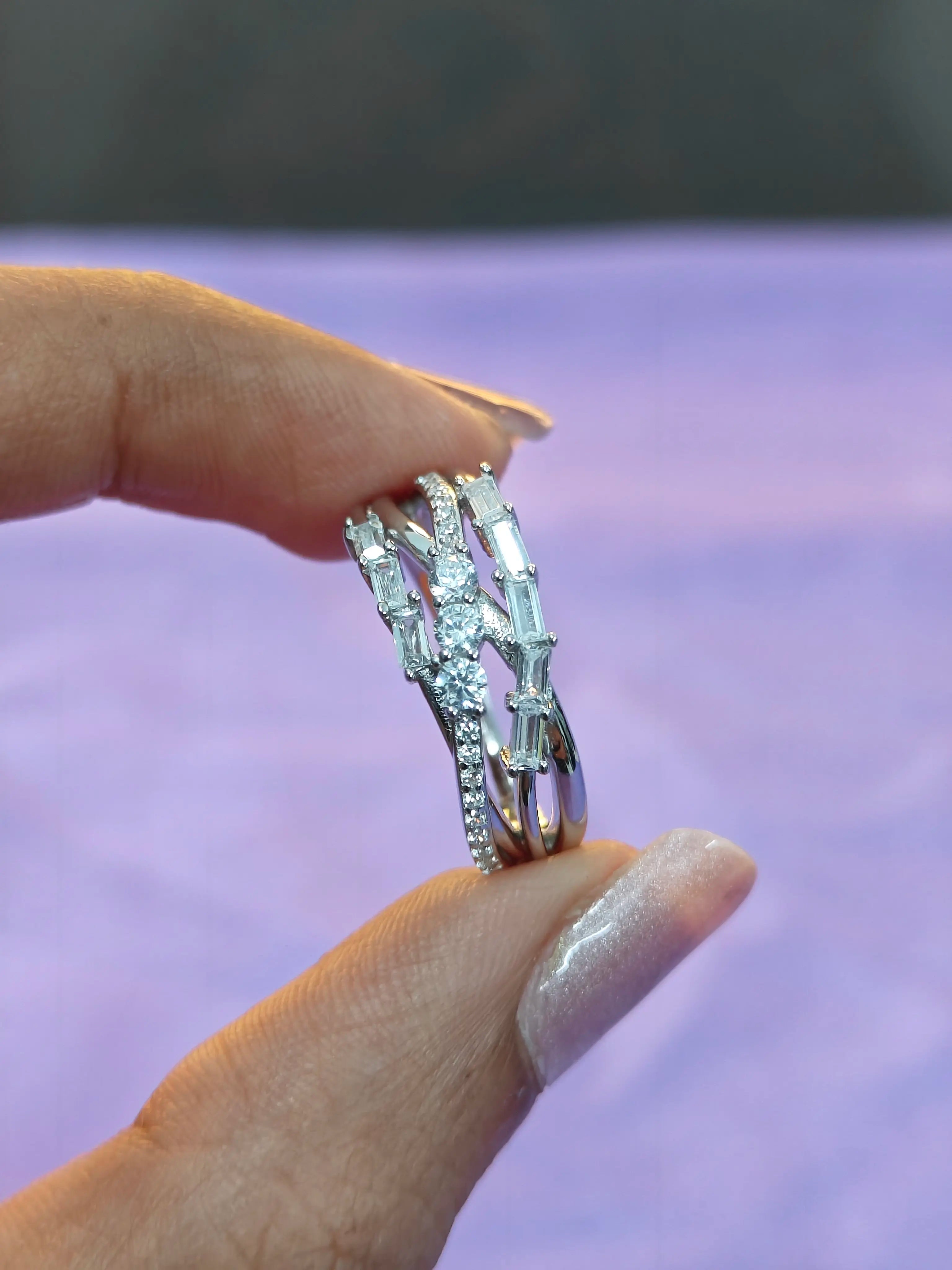 Silver ring with gemstones held by a hand against a blurred purple background