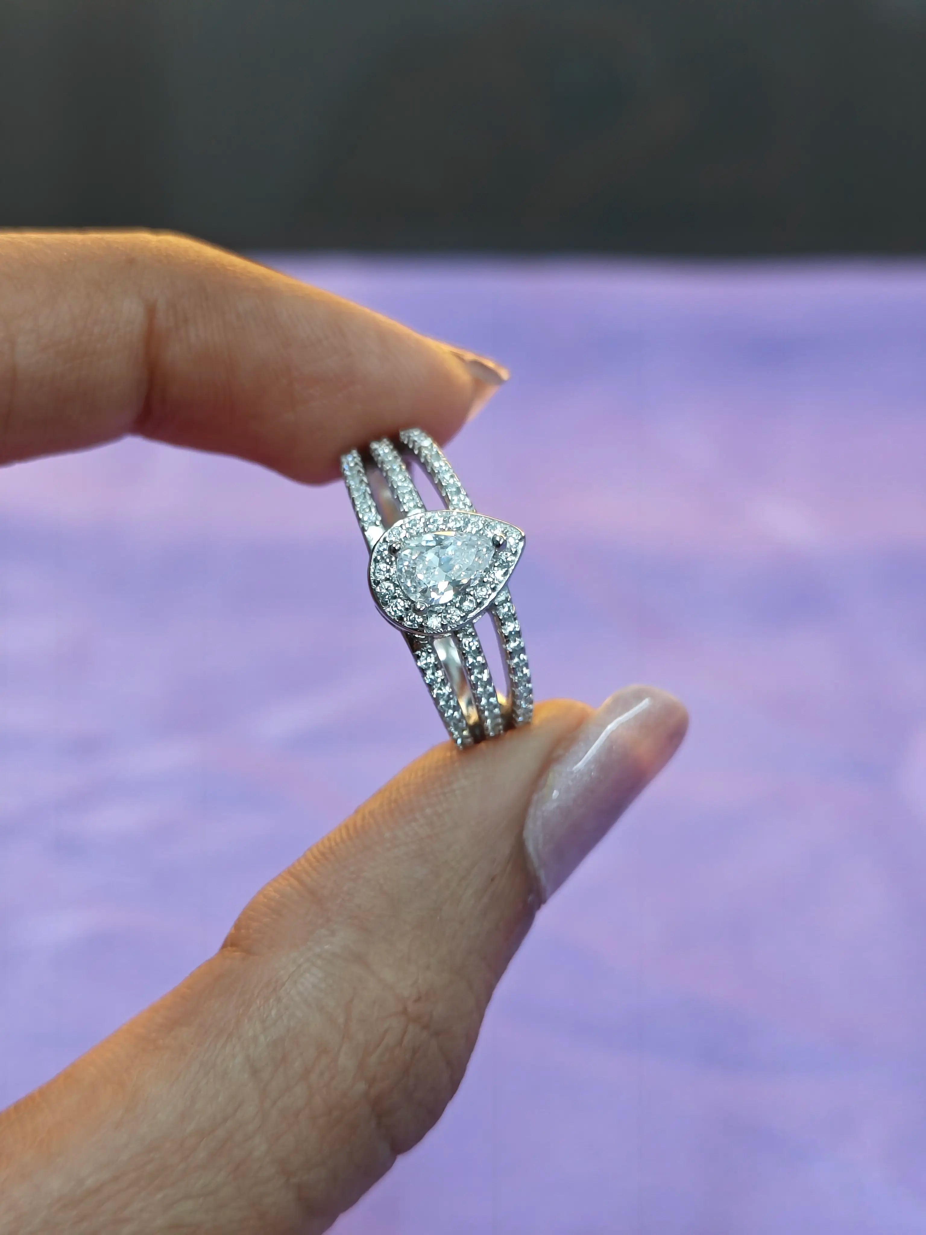 Silver ring with a large central gemstone held between fingers against a blurred background