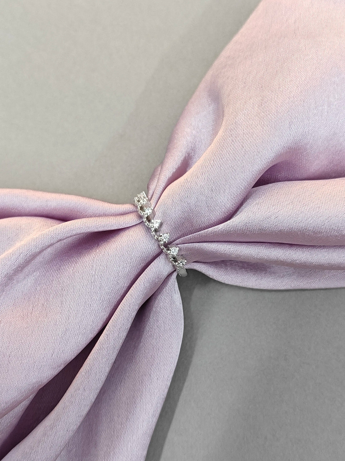 Close-up of a pink fabric bow with a decorative brooch on a light gray background