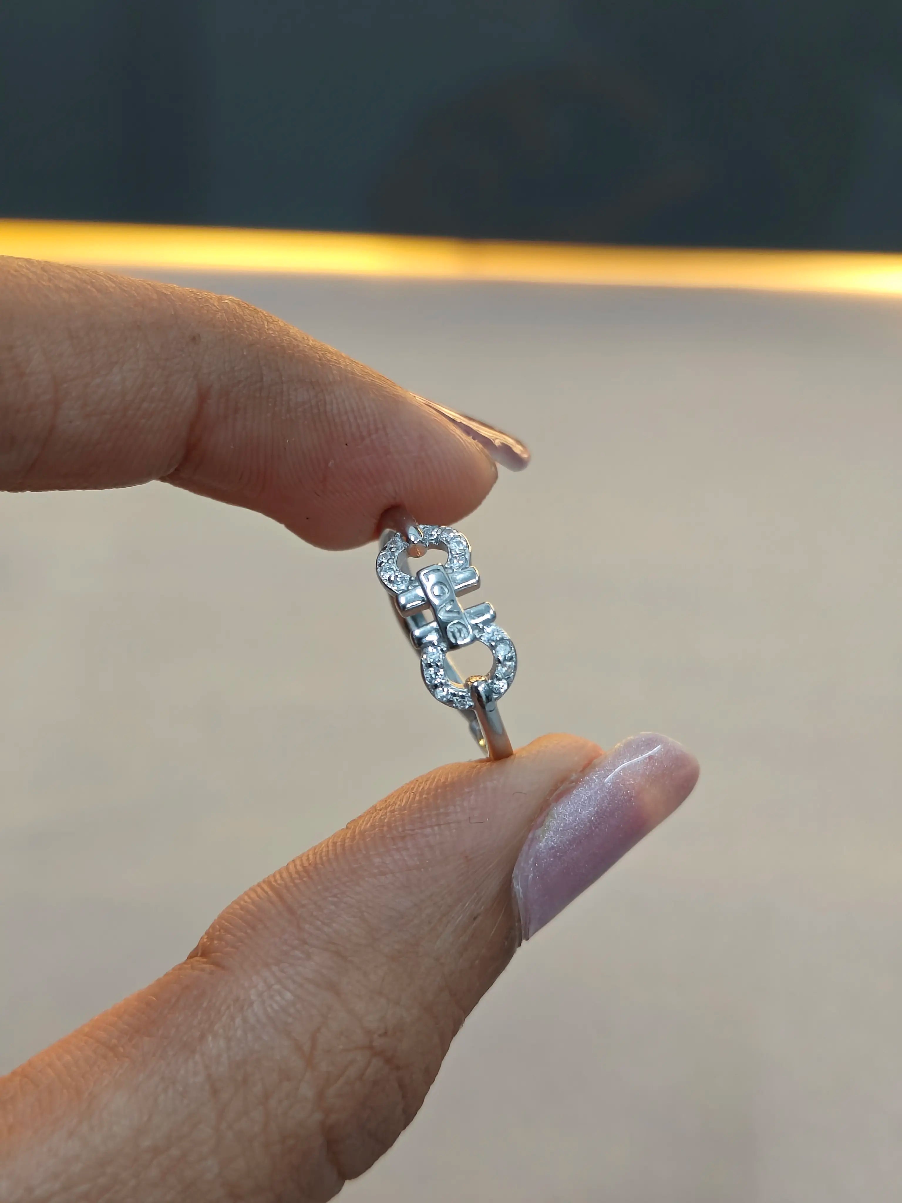 Silver ring with a unique design held between fingers against a blurred background