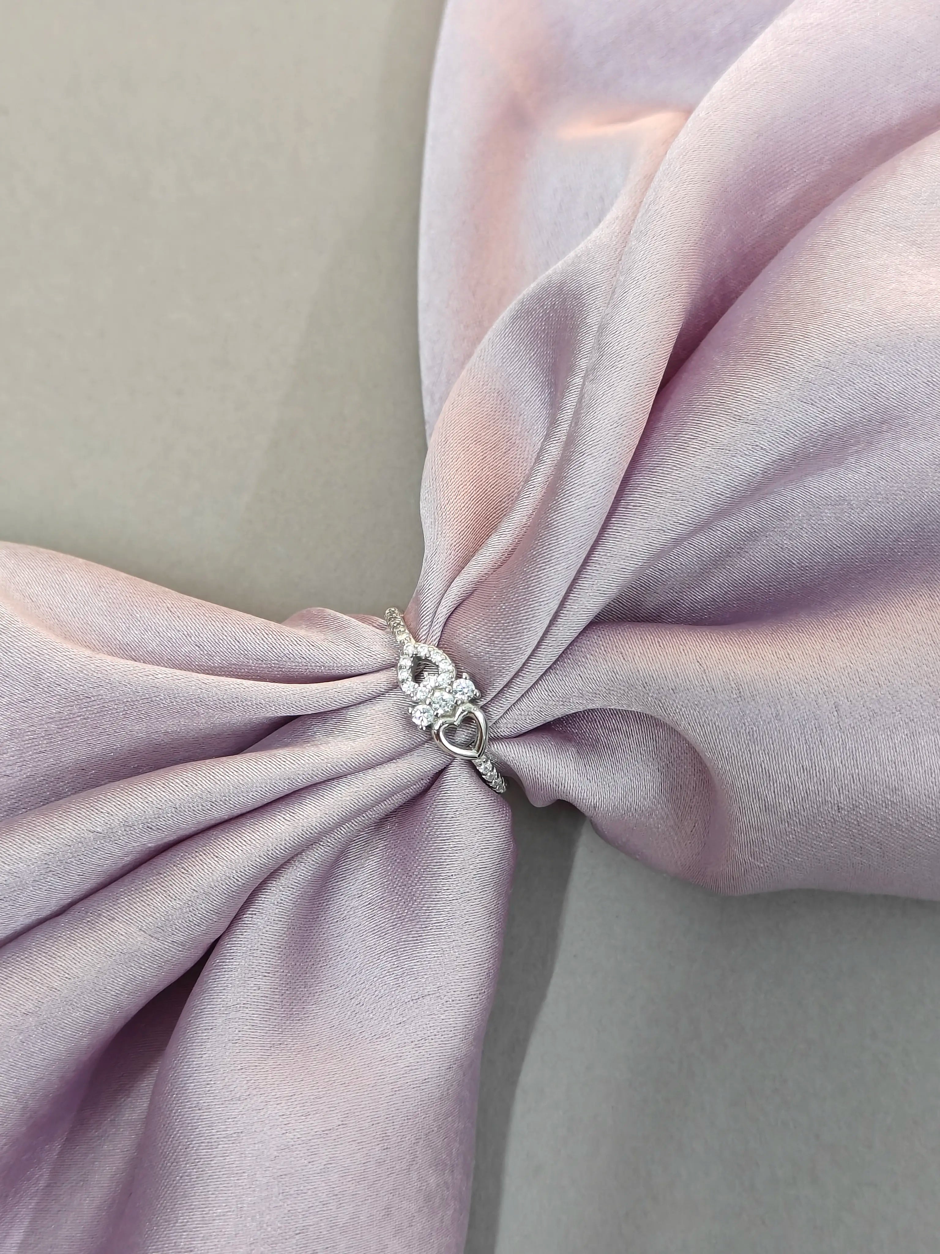 Close-up of a pink fabric bow with a decorative brooch on a matching background