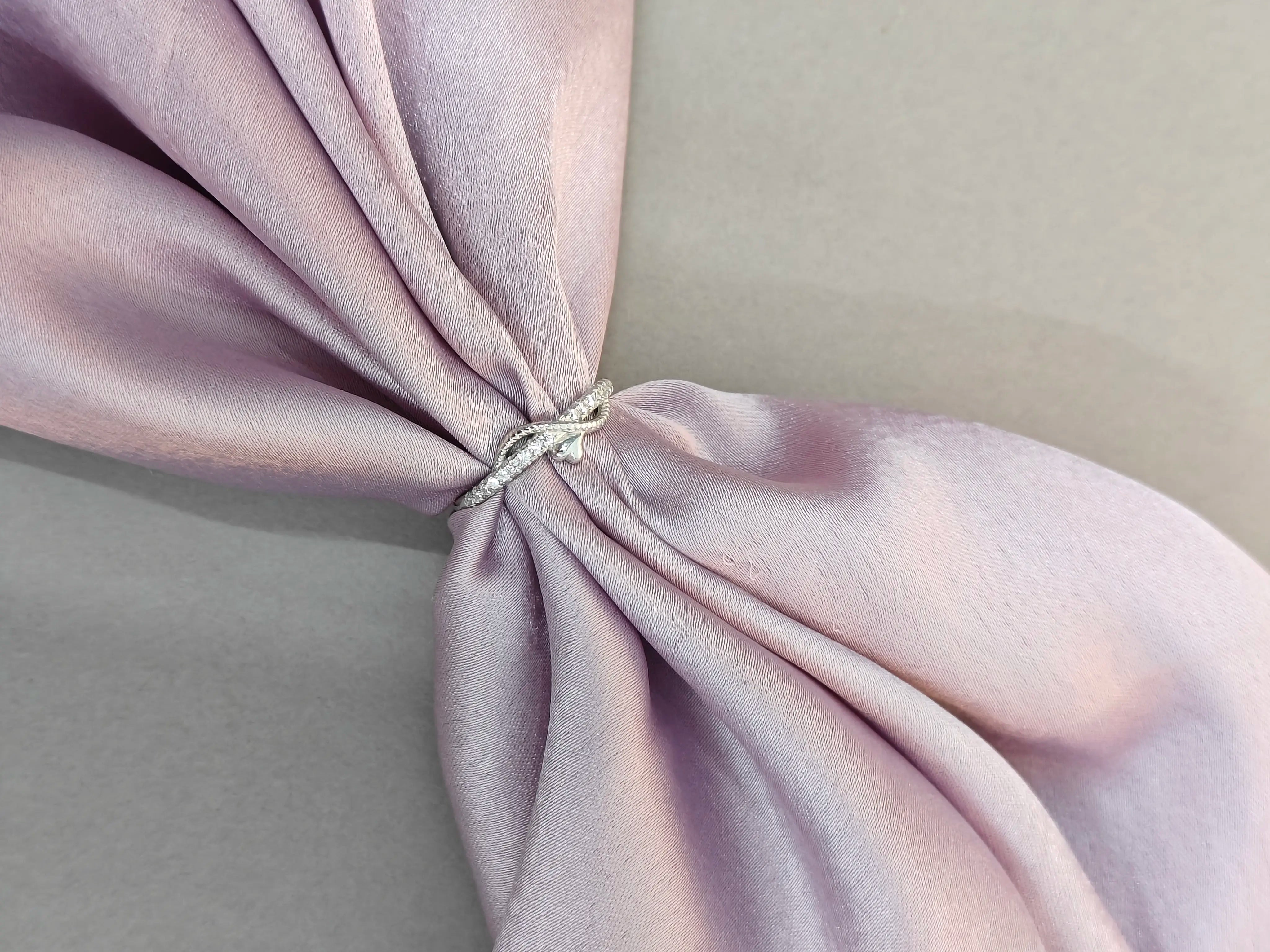 Close-up of a silver ring on a knotted pink fabric with a neutral background