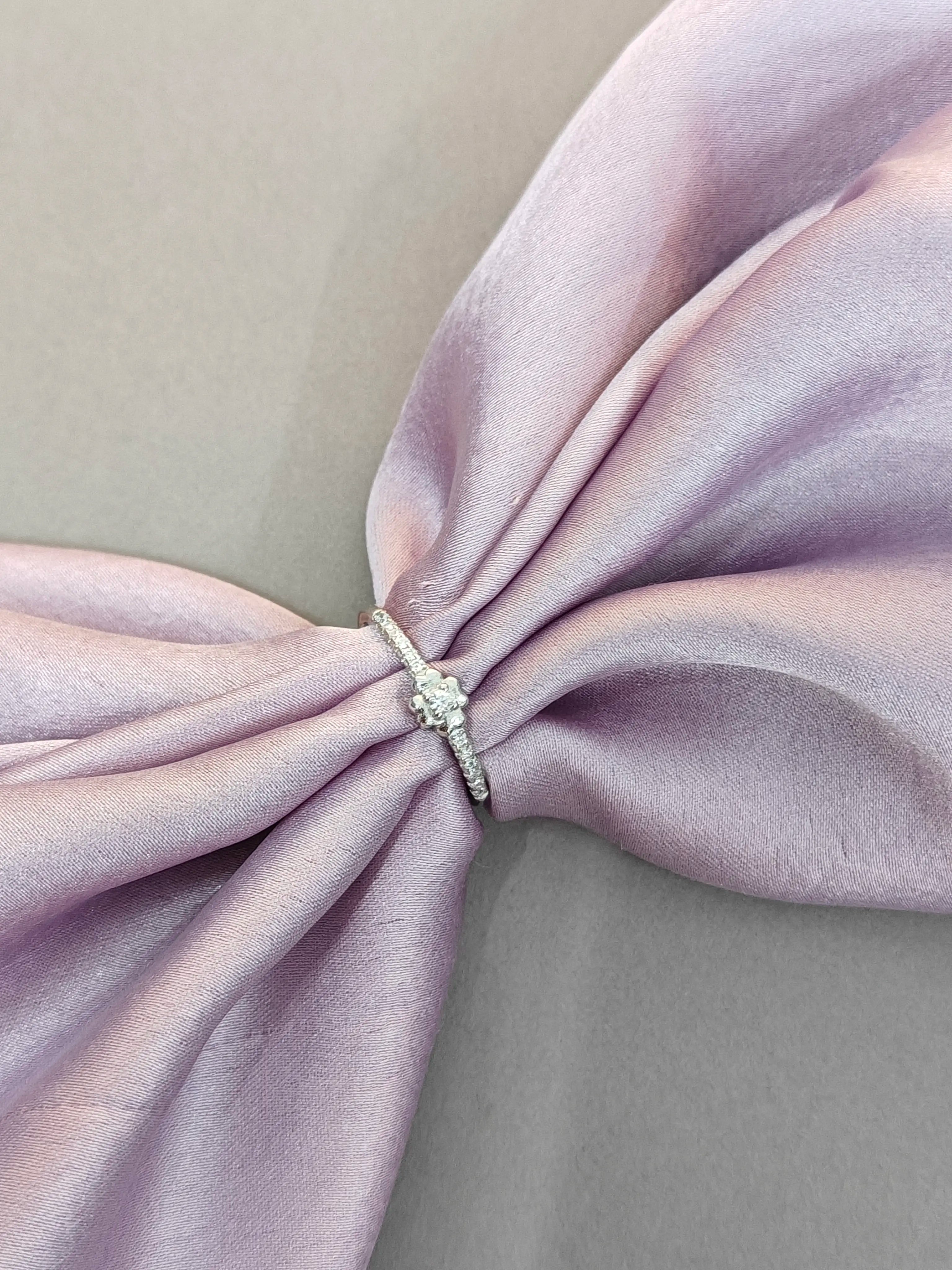 Diamond ring on a pink satin bow with a neutral background