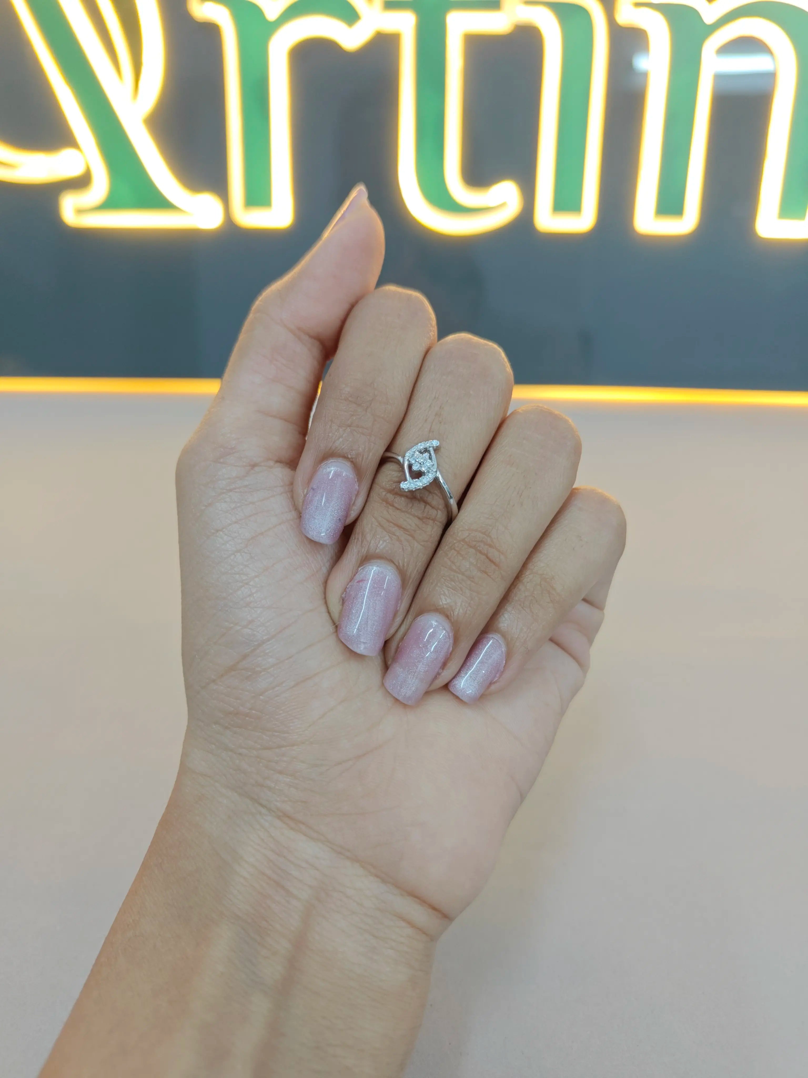 Hand wearing a diamond ring with a neon sign in the background